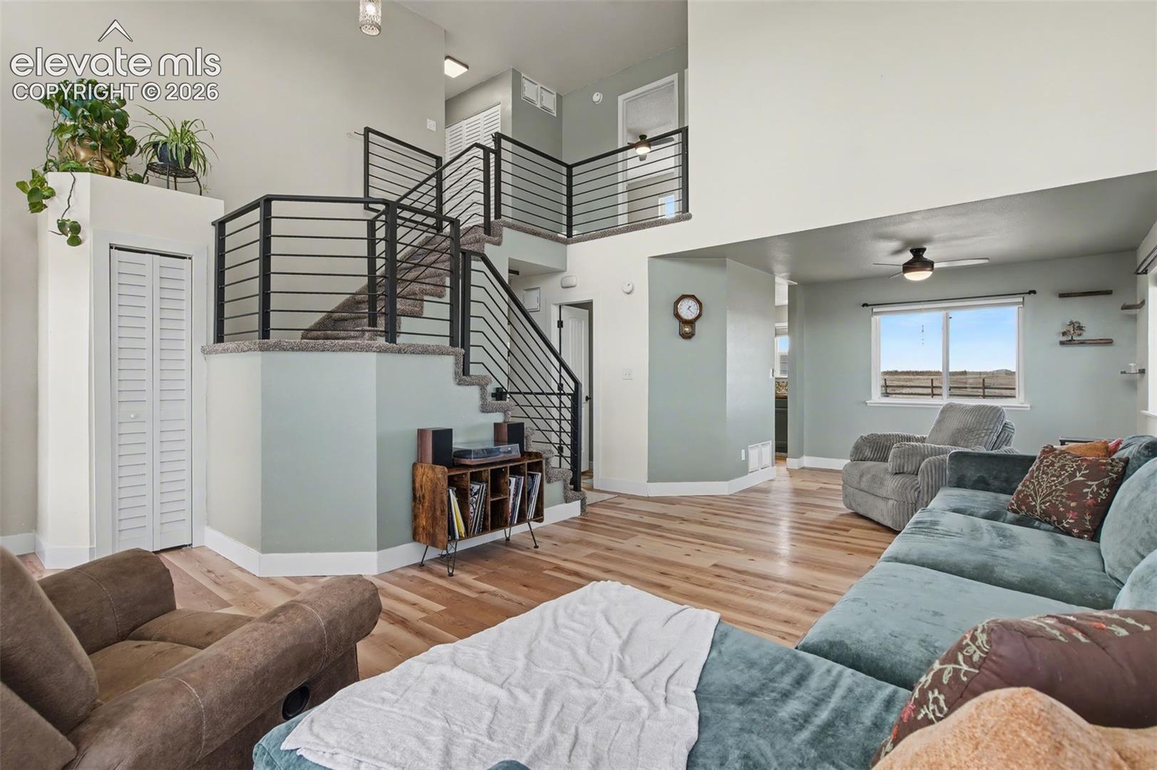 Open floor plan featuring vaulted ceilings, wood-finish flooring, and a staircase with a horizontal metal railing system