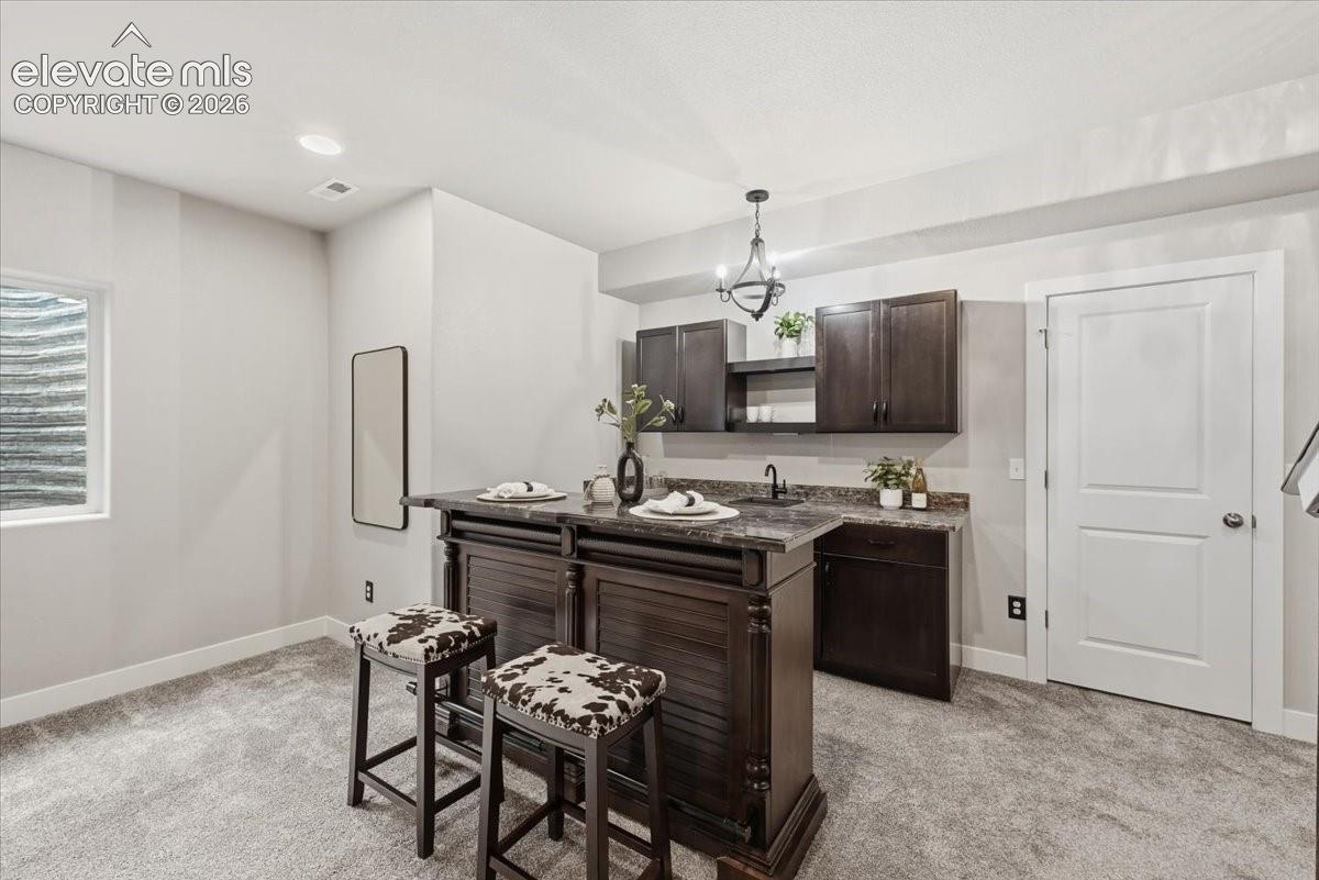 Built-in wet bar featuring dark wood-finish cabinetry, stone-finish countertops, and an integrated sink with a matte black faucet