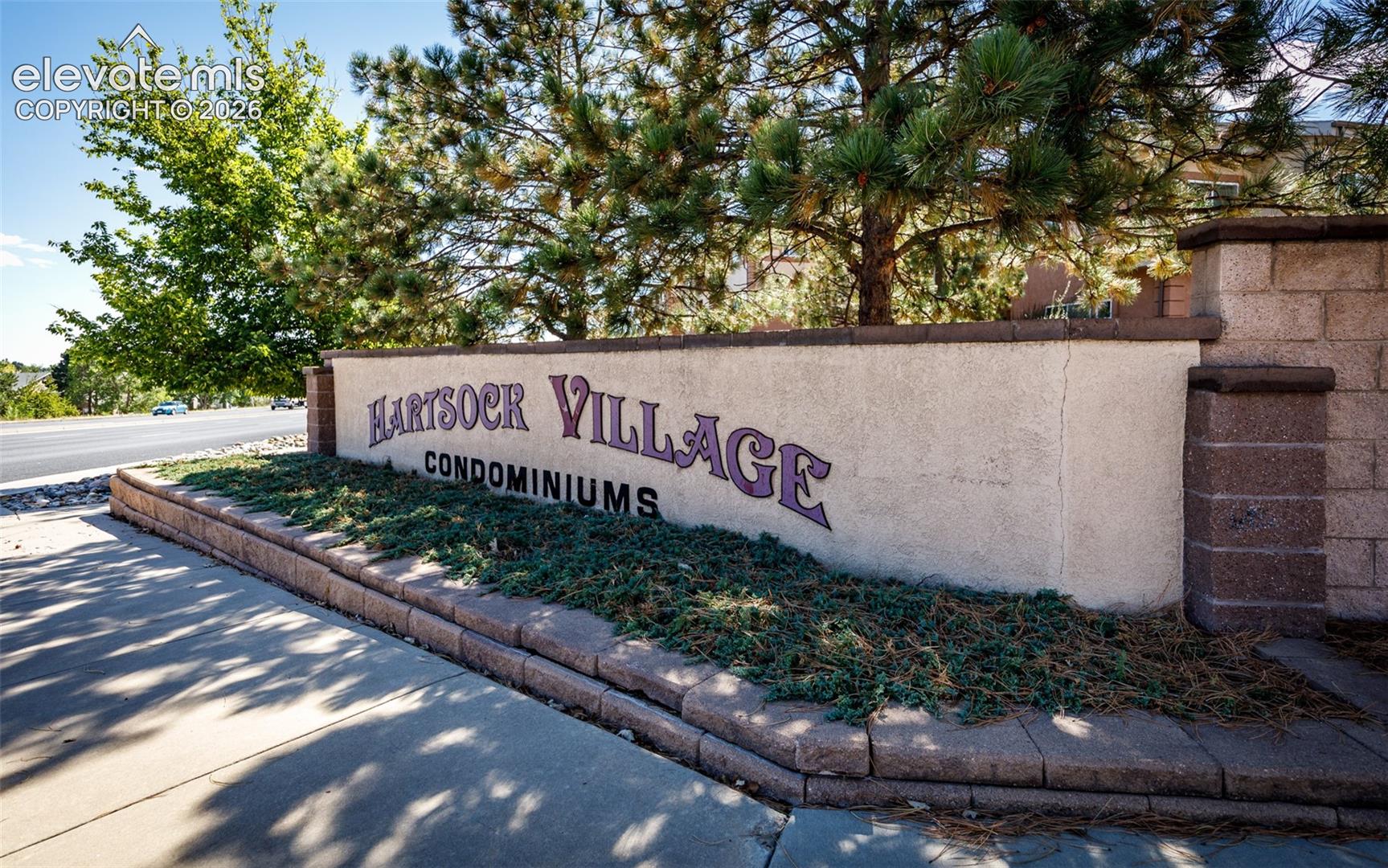 Stucco and masonry monument signage featuring decorative lettering, accented by concrete curbing and manicured evergreen shrubbery