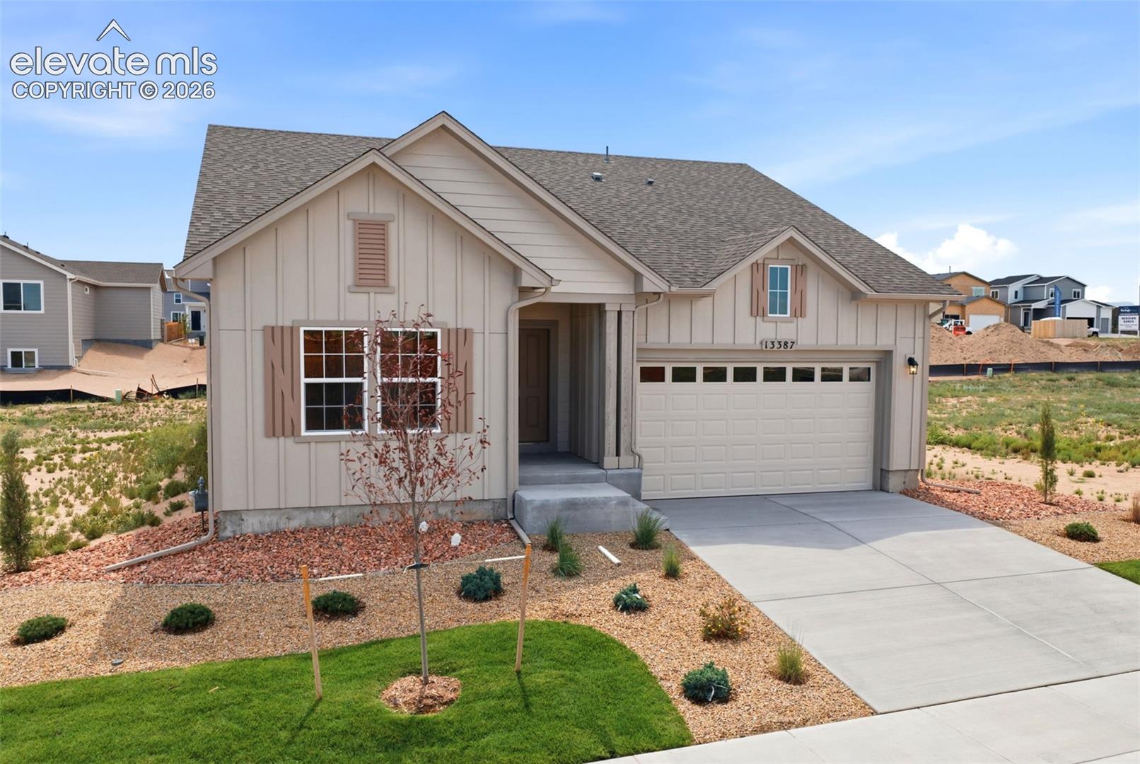 Single-story residence featuring vertical siding, decorative shutters, a concrete driveway, an attached two-car garage, and low-maintenance xeriscaping