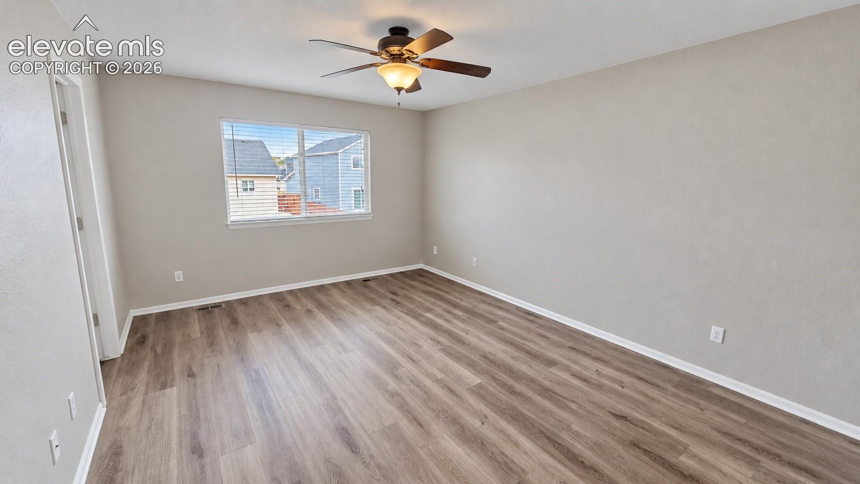 Neutral-toned interior room featuring wood-finish flooring, a ceiling fan with integrated lighting, and a single-pane window