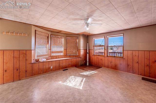 Carpeted empty room with a ceiling fan, wooden walls, and wainscoting