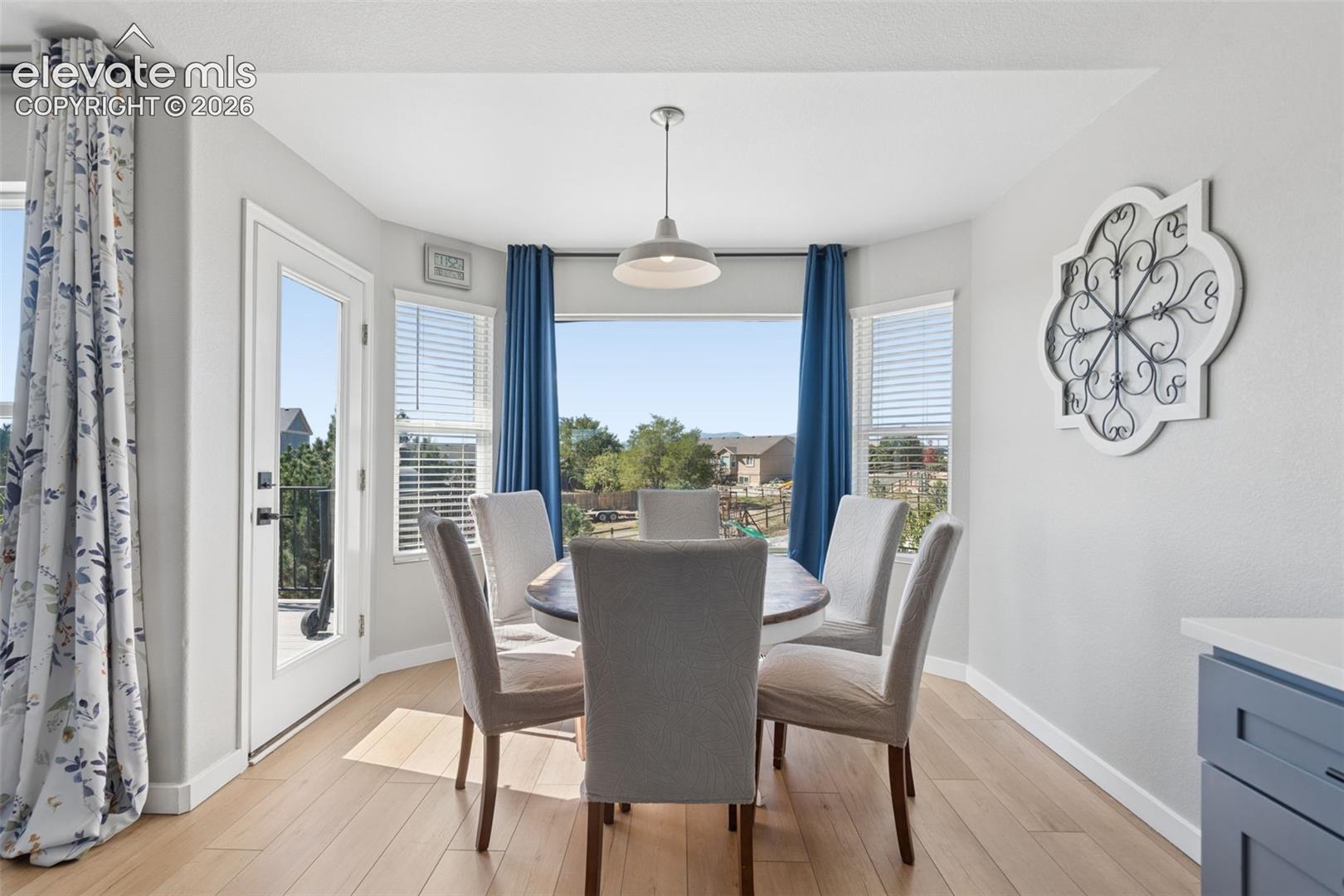 Bay window dining area with light luxury vinyl flooring, a pendant light fixture, and white trim