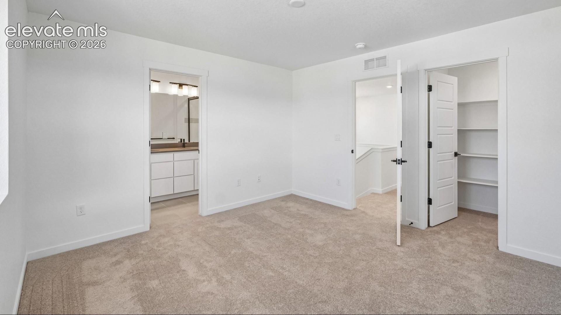 Neutral-toned wall-to-wall carpeting, walk-in closet with built-in shelving, and six-panel interior doors