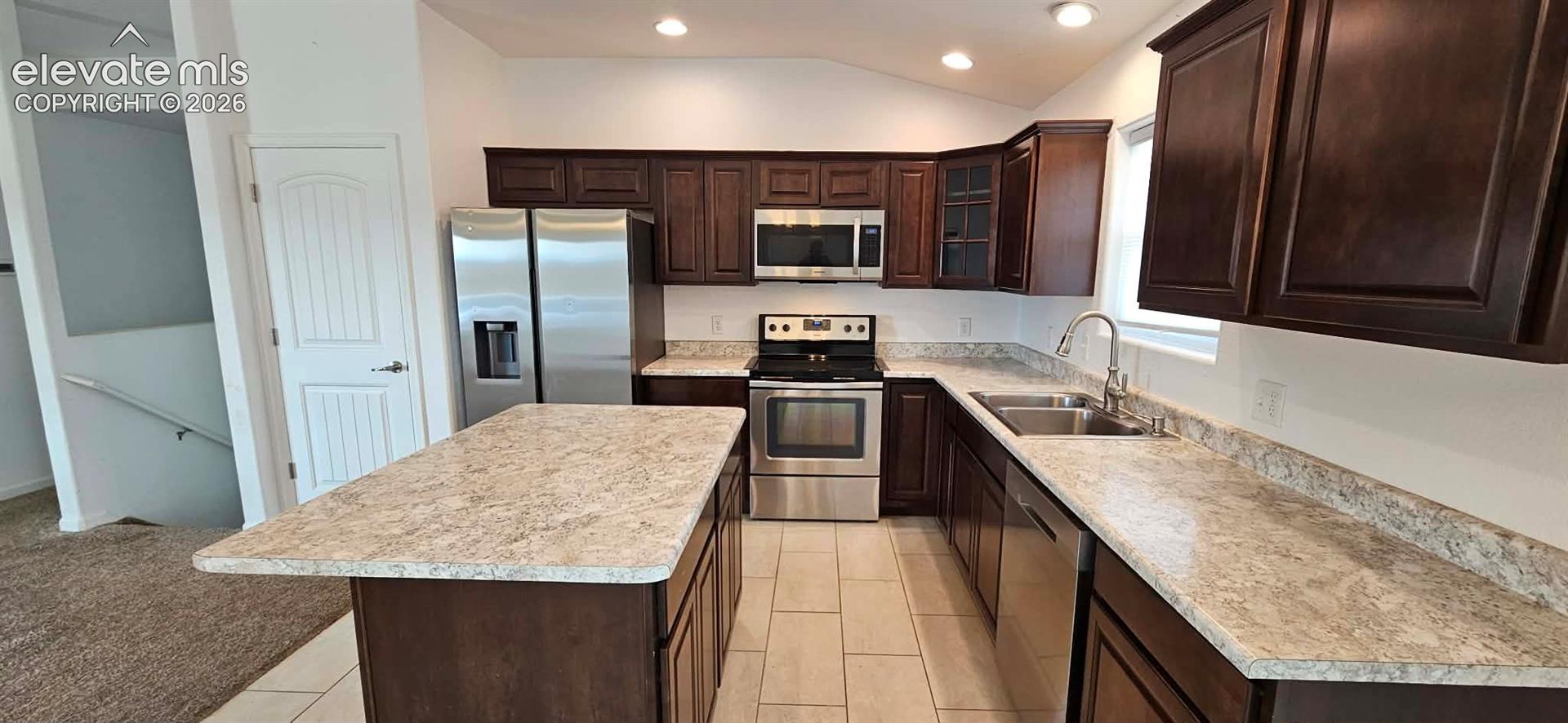 Kitchen featuring dark-finish cabinetry, stone-patterned countertops, a central island, stainless steel appliances, and tile flooring
