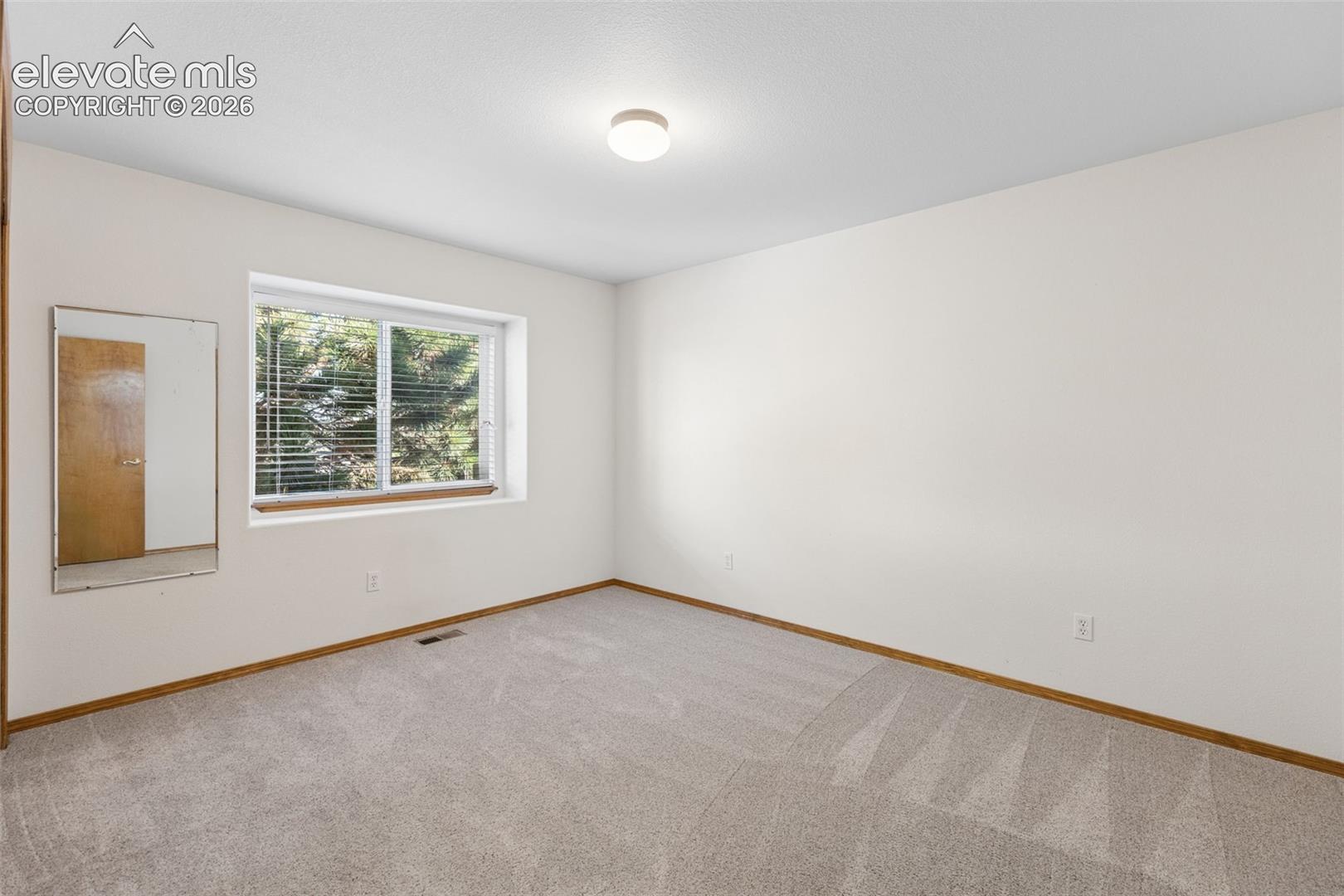 Neutral wall-to-wall carpeting, window with integrated blinds, flush-mount ceiling light fixture, and wall-mounted mirror