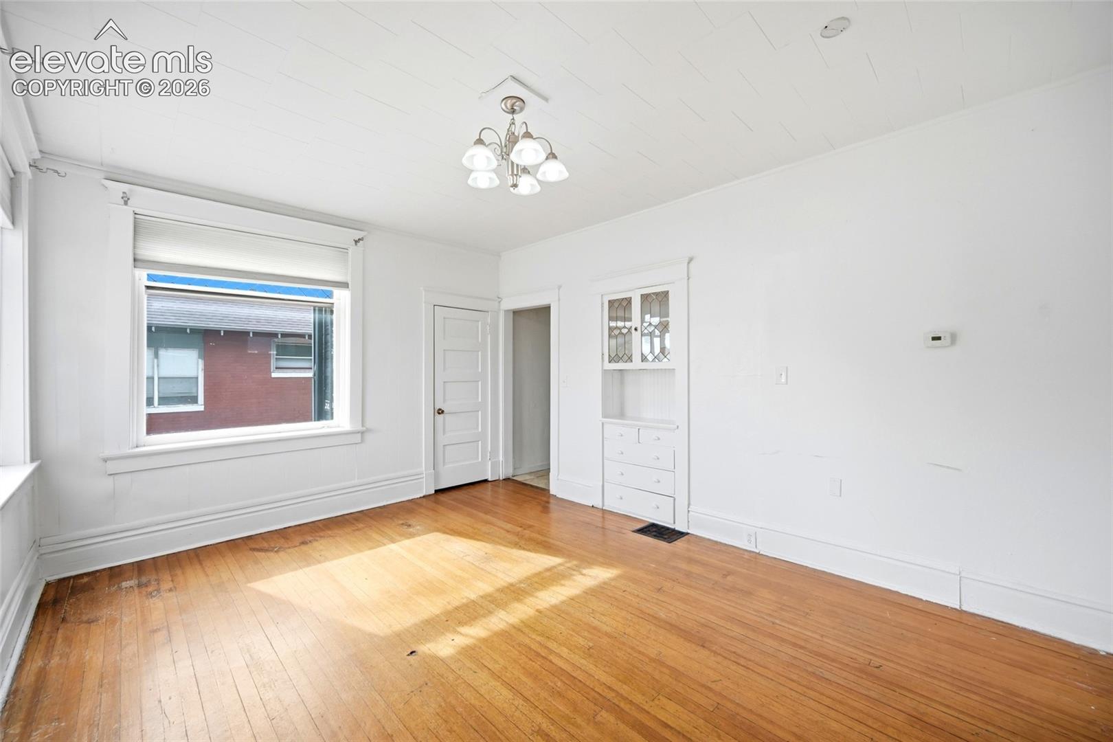 Interior space featuring wood-finish flooring, a multi-pane glass-front built-in cabinet, a five-arm chandelier, and a five-panel interior door