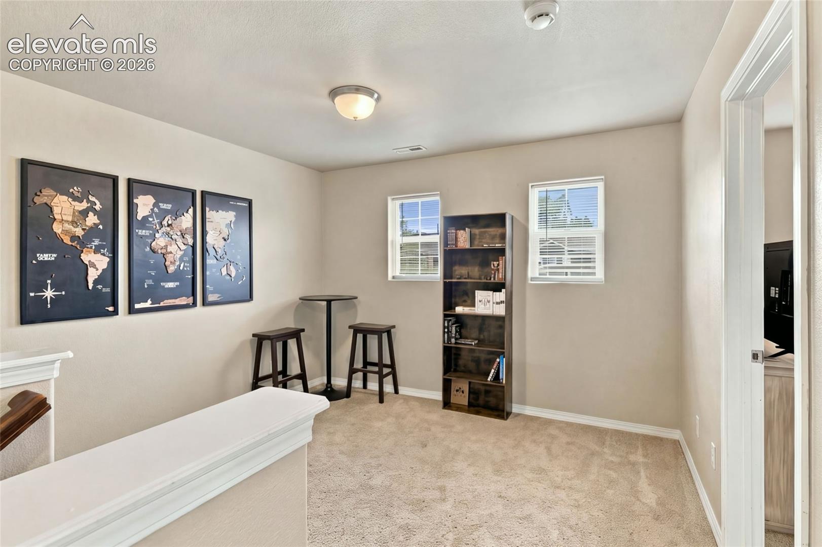 Neutral-toned interior space featuring wall-to-wall carpeting, dual windows, and a semi-partitioned wall with a capped ledge