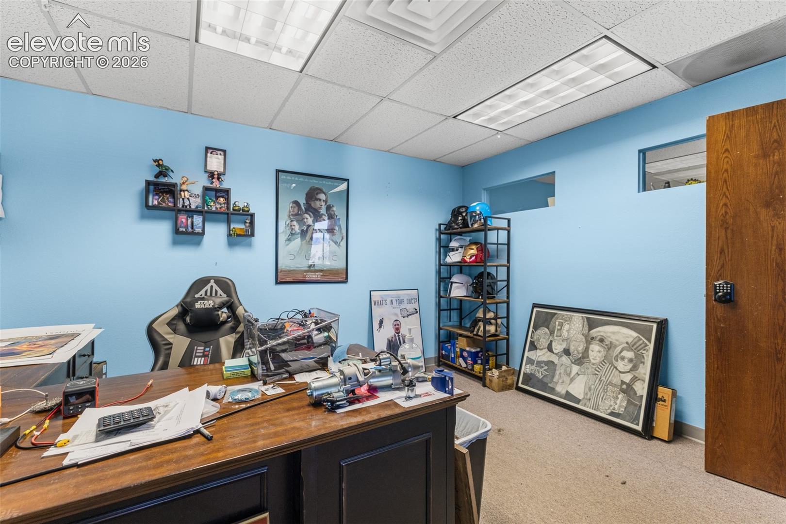Interior room featuring recessed wall niches, acoustic drop ceiling tiles, rectangular fluorescent lighting fixtures, and a solid wood door with electronic keypad hardware