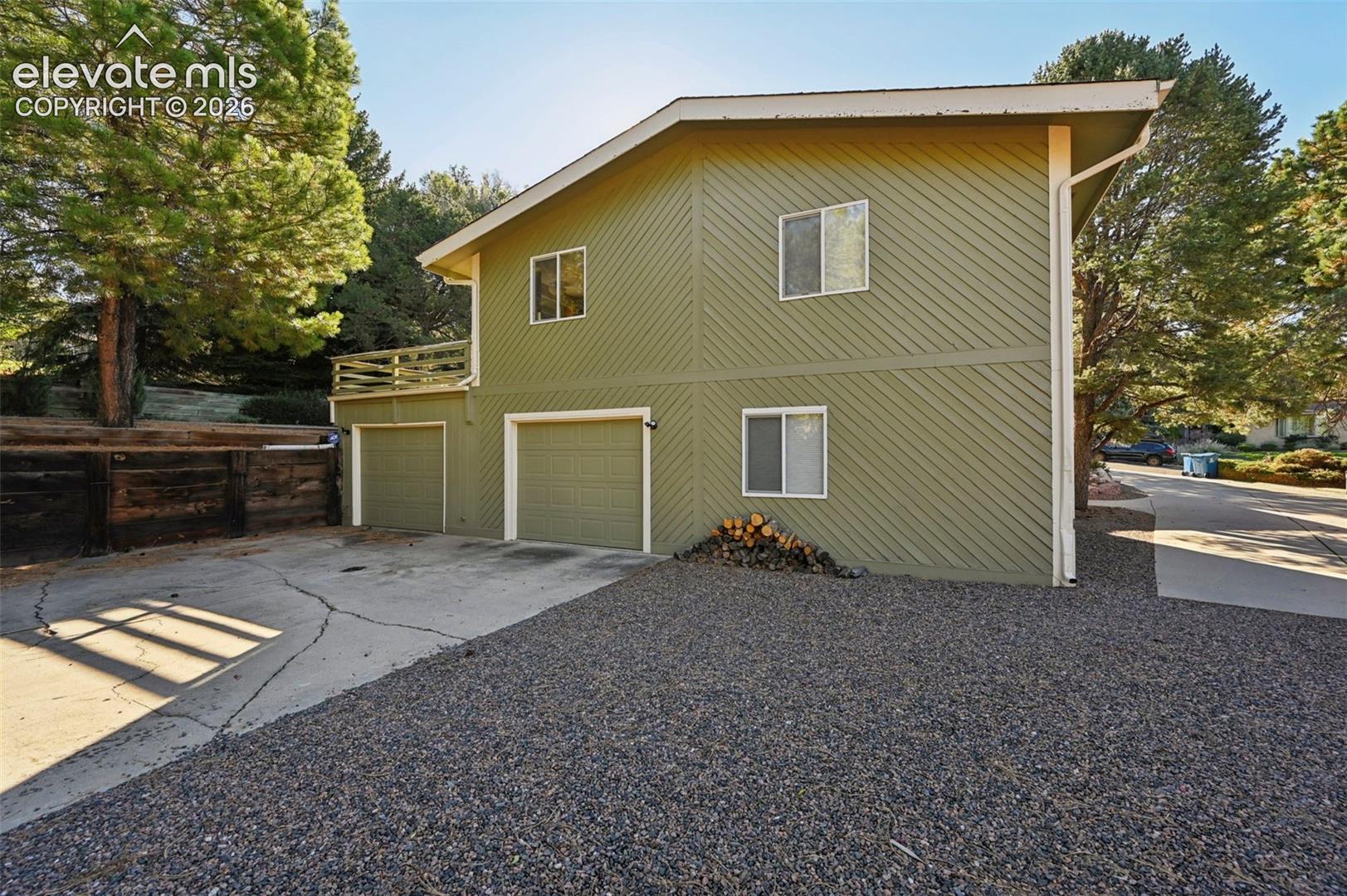Two-story exterior featuring diagonal wood siding, attached double garage, concrete driveway, and elevated wood-rail balcony