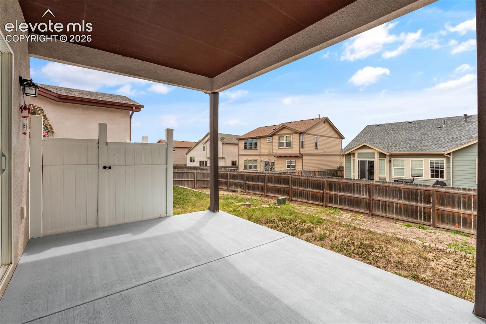 Covered concrete patio featuring an exterior wall-mounted light fixture, a vinyl privacy partition, and a fenced rear yard