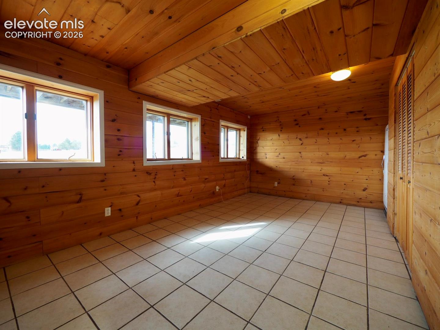 Interior space featuring tongue-and-groove wood wall paneling, matching wood ceiling planks, ceramic tile flooring, and multiple casement windows with light-toned frames