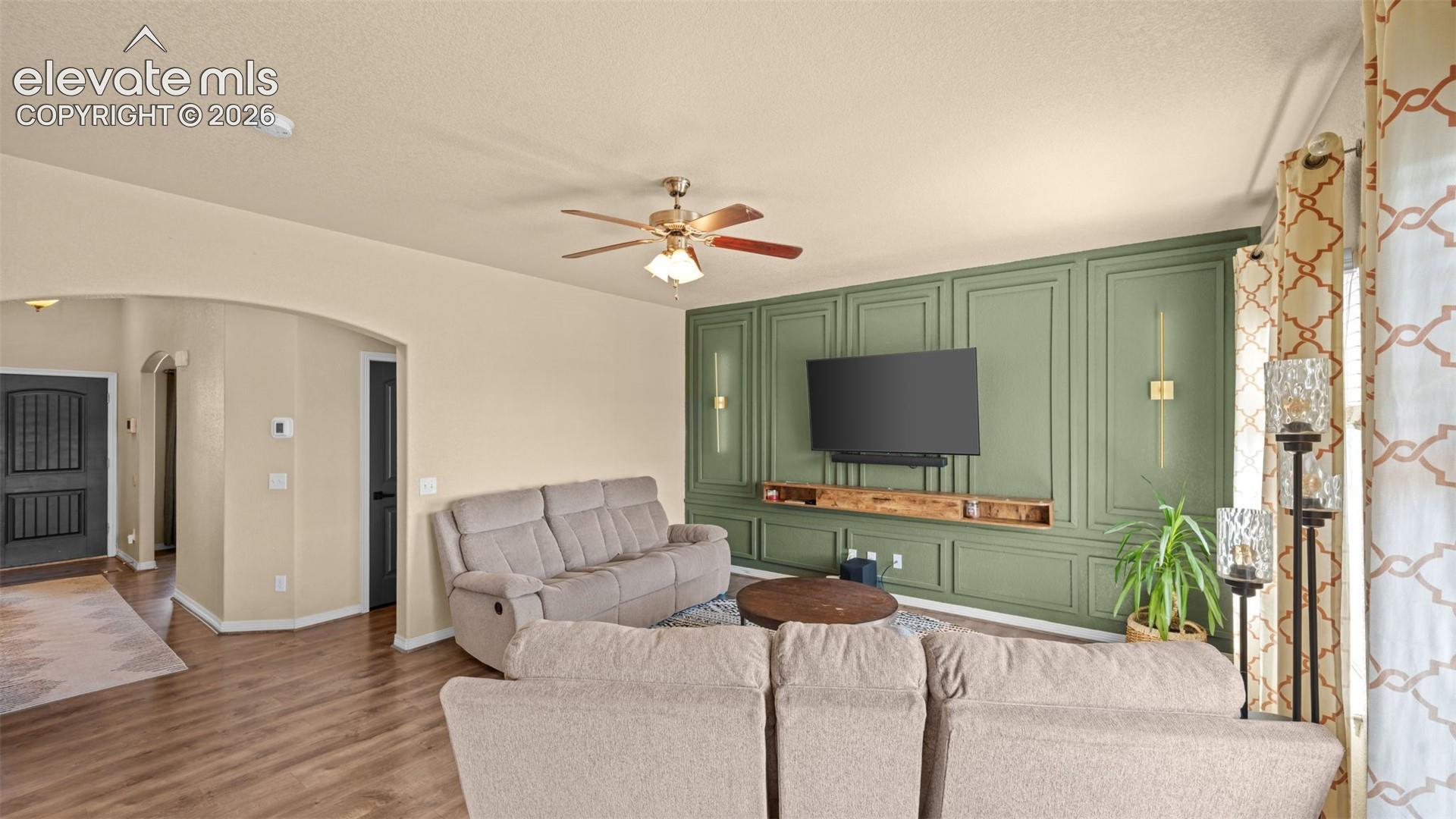 Living area featuring a sage green accent wall with decorative molding and integrated sconce lighting