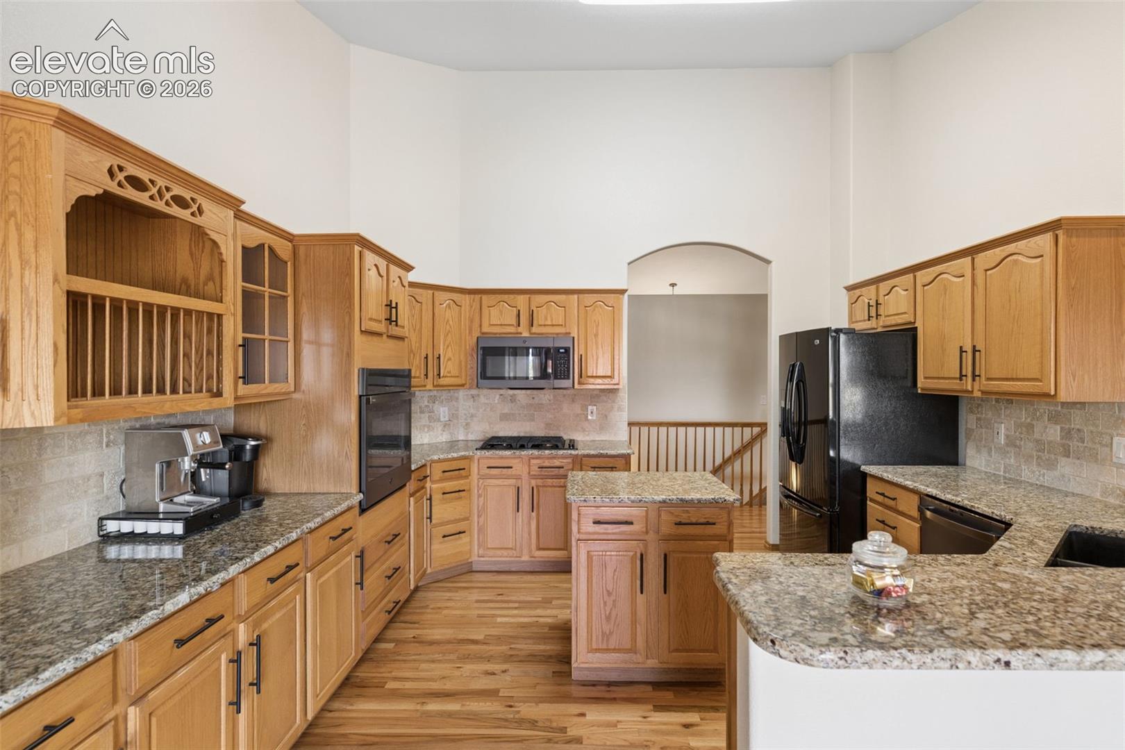 Kitchen featuring high ceilings, wood-finish flooring, custom wood cabinetry, stone countertops, and a central island