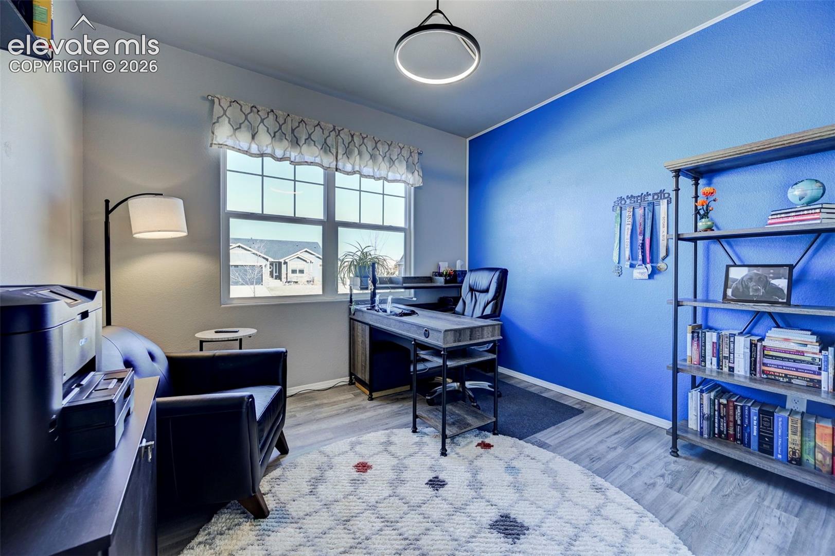 Bright interior room featuring a large window with gridded panes, light wood-finish flooring, and a contemporary ceiling light fixture