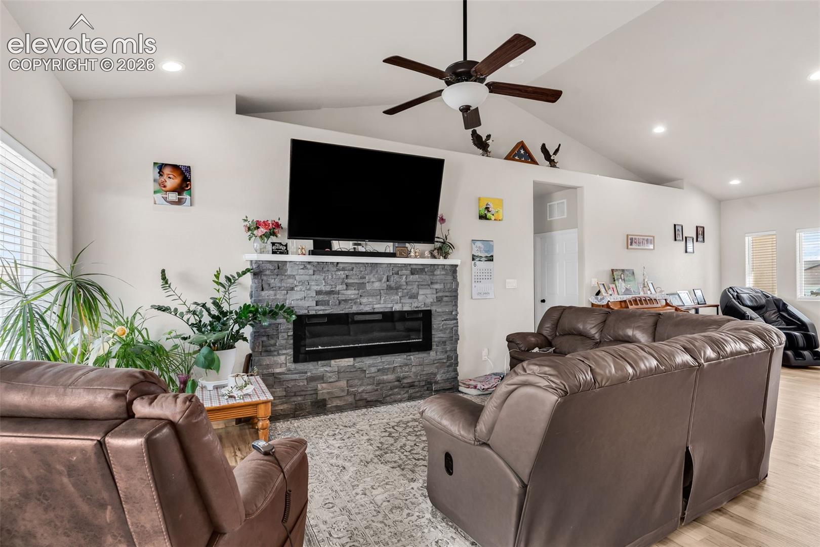 Living area featuring a stone-clad fireplace with an integrated electric insert, a mounted television, and a ceiling fan with light fixture
