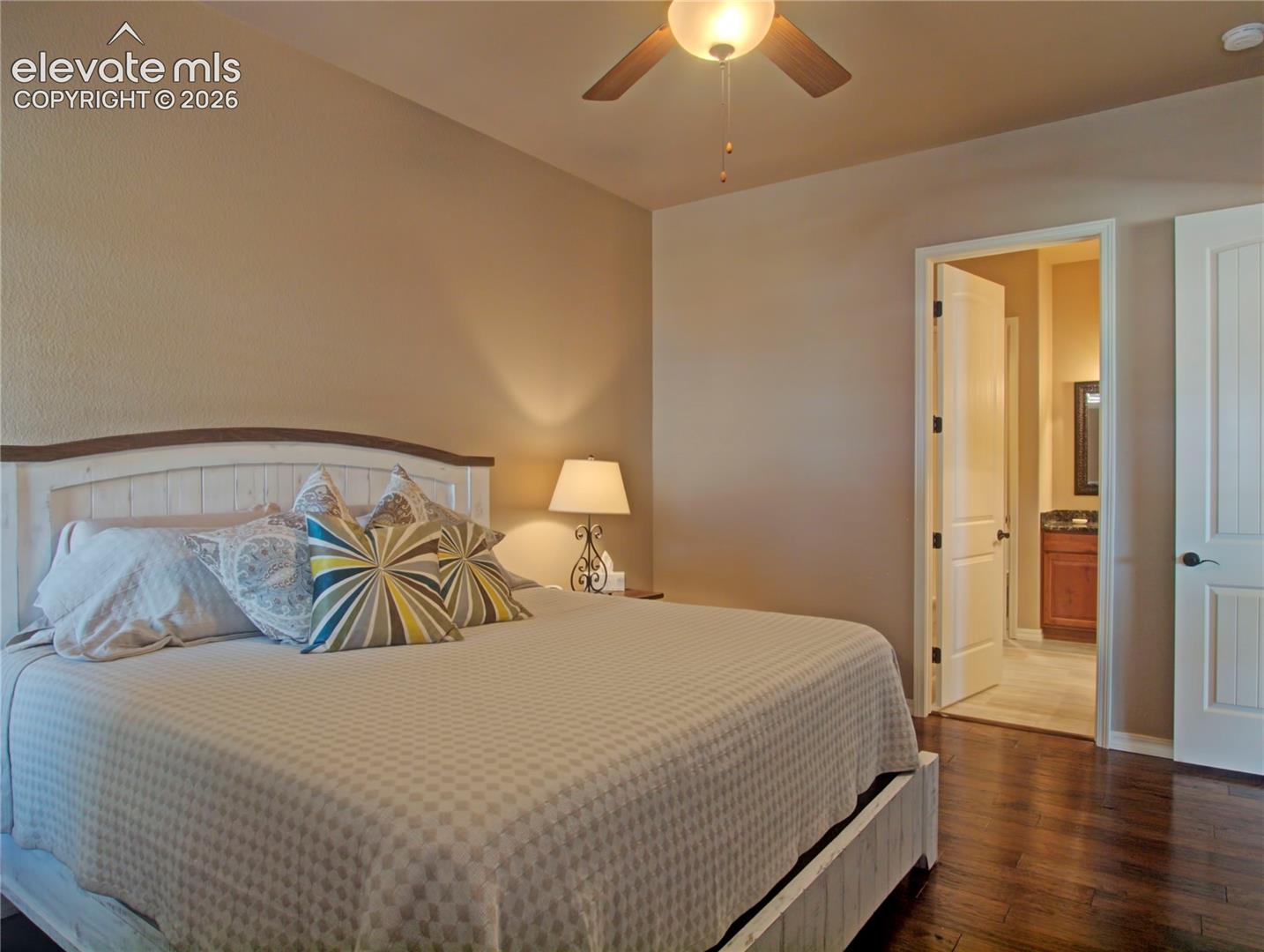 Bedroom featuring dark wood-finish flooring, a ceiling fan with integrated lighting, and neutral wall tones. Attached on suite and walk in closet.