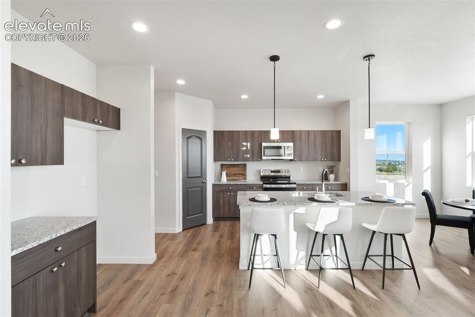 Open-concept kitchen featuring wood-finish cabinetry, a central island with bar seating, stainless steel appliances, and recessed lighting