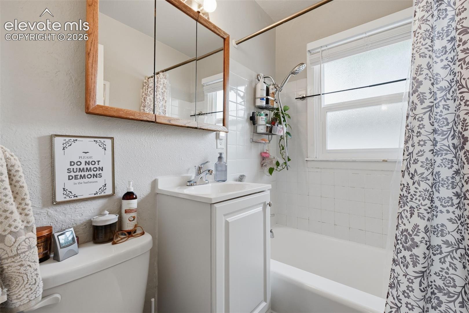 White vanity with integrated sink, wood-framed medicine cabinet, and white tile shower surround