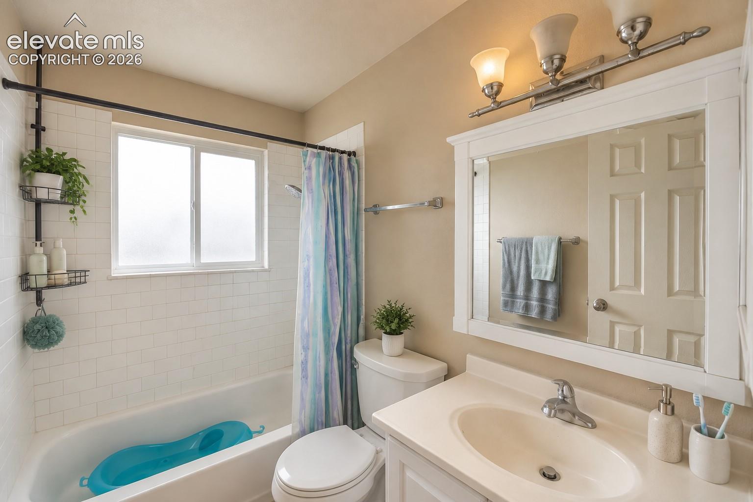 White subway tile surround, built-in bathtub, vanity with integrated sink, framed mirror, and brushed nickel light fixture