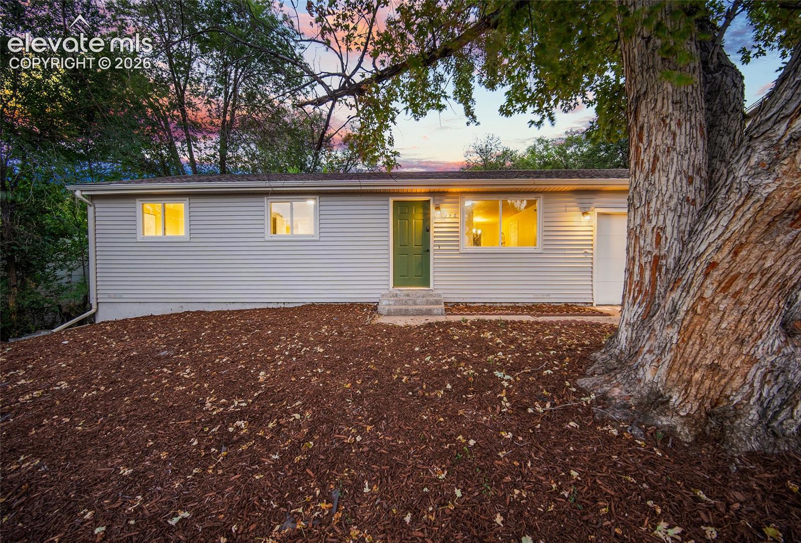Siding exterior with multiple windows, prominent mature tree, deep green entry door, and attached garage