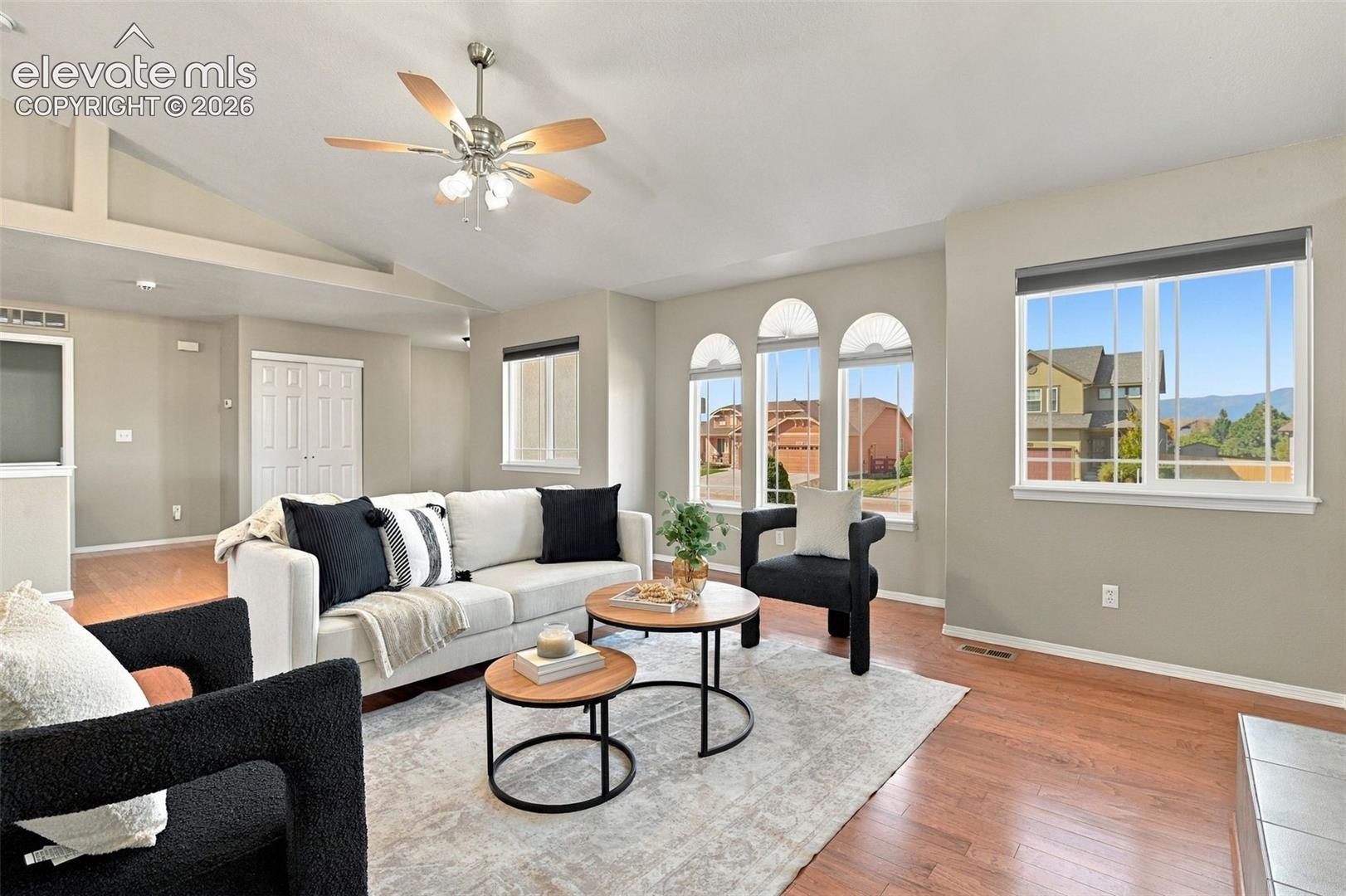 Vaulted ceilings with a ceiling fan, wood-finish flooring, multiple arched windows, and white interior doors