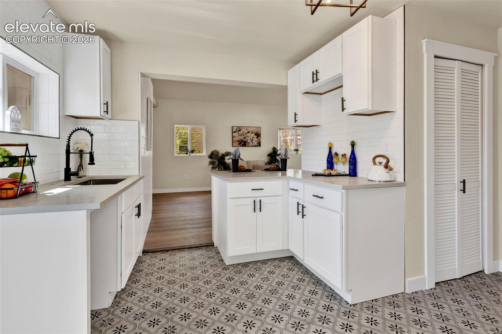 Kitchen featuring patterned floor tiles, white cabinetry with matte black hardware, light-toned countertops, and a white subway tile backsplash