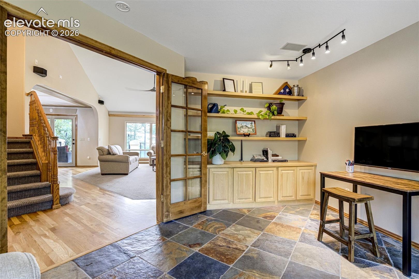 Slate tile flooring, custom built-in cabinetry, floating wood shelving, track lighting, and wood-frame French doors