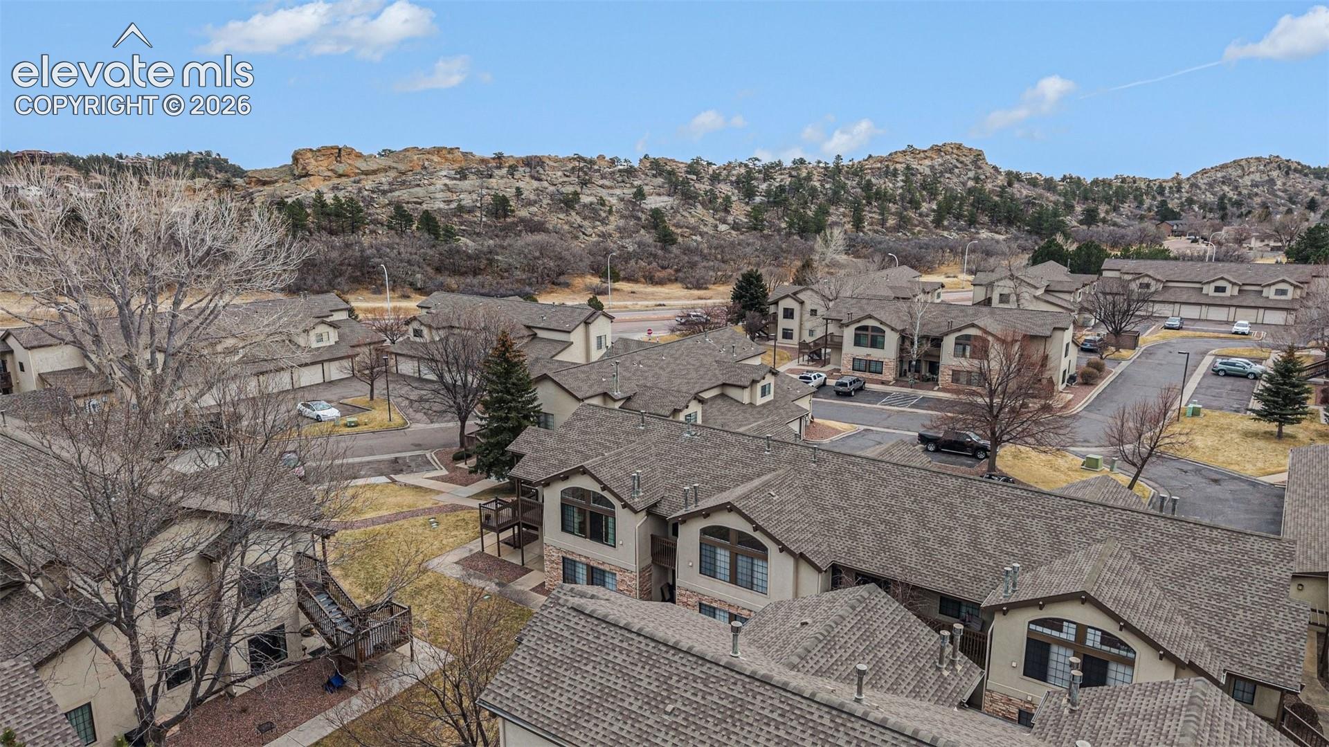 Aerial perspective of a multi-unit residential community featuring pitched shingle roofing, stucco siding, stone veneer accents, and arched window detailing with a mountainous backdrop