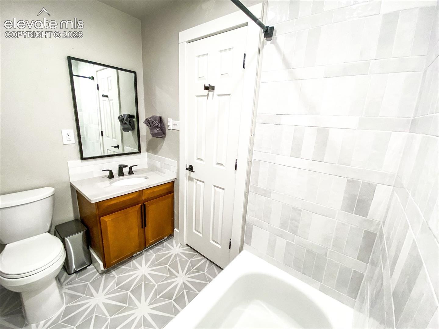 Bathroom featuring a white bathtub, patterned floor tile, wood-finish vanity with countertop, and a vanity mirror
