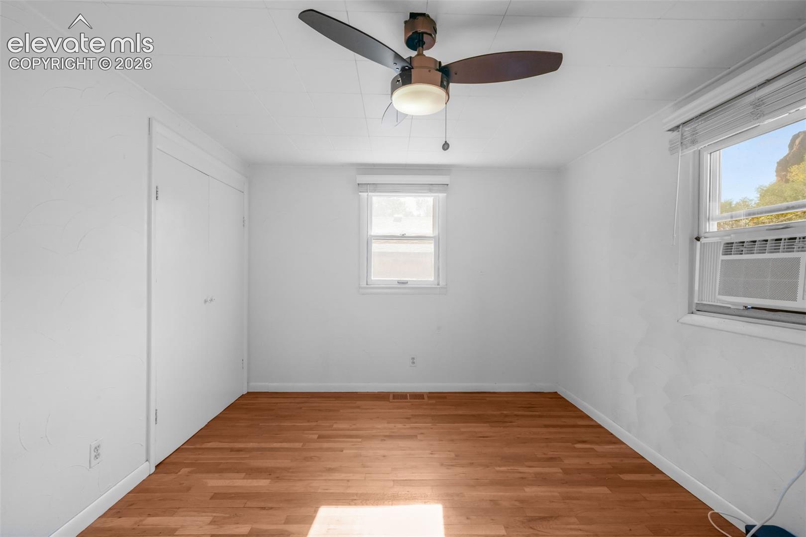 Hardwood flooring, white walls, two windows, ceiling fan, and built-in closet