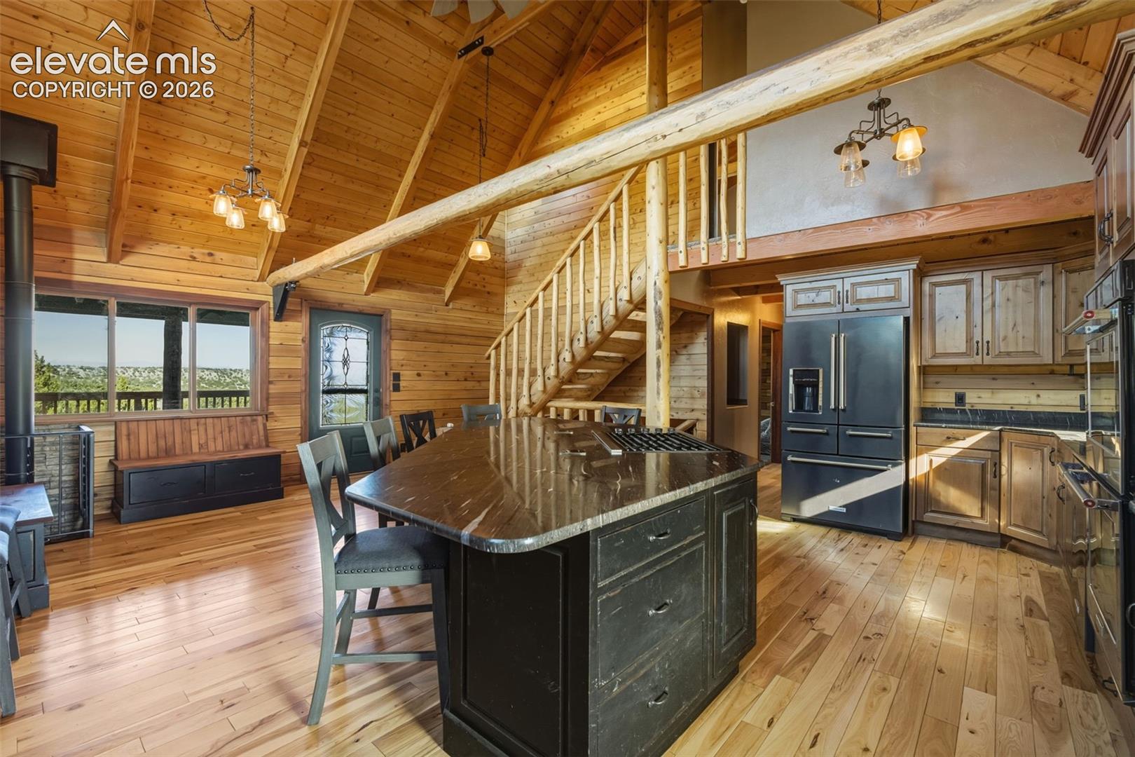 Open-concept living space with vaulted wood-paneled ceilings, a central kitchen island with a dark countertop, stainless steel appliances, and wood-finish flooring