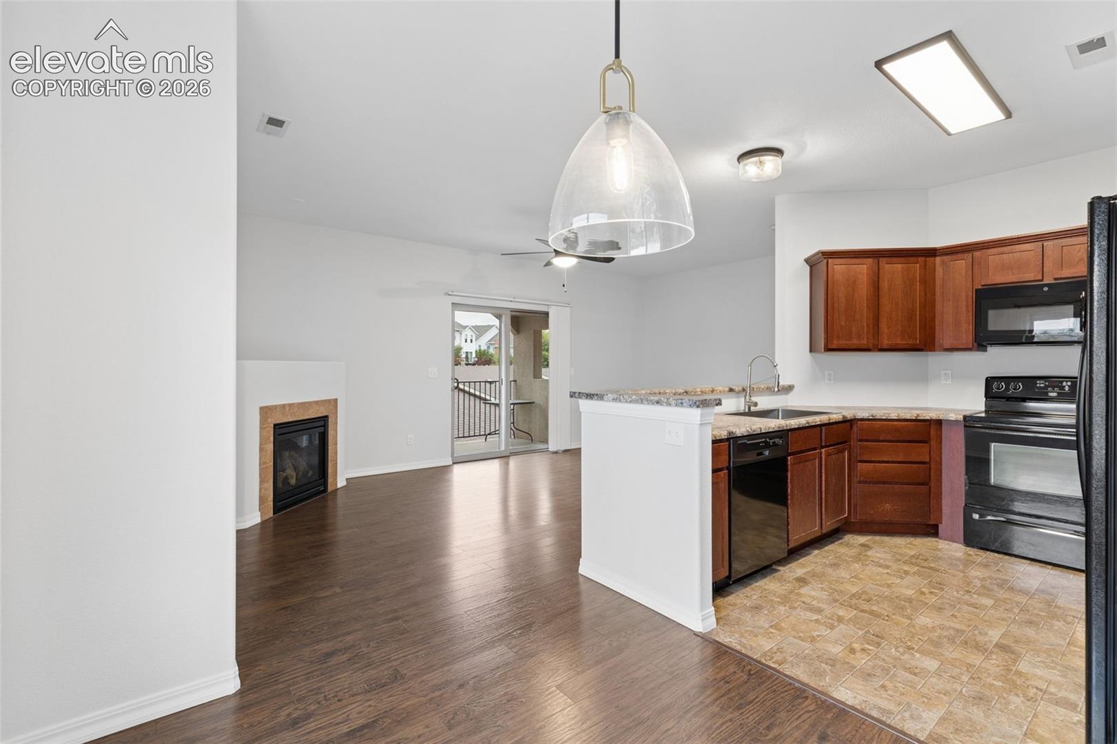 Kitchen featuring wood cabinetry, stone-finish countertops, and built-in appliances, alongside a living area with wood-finish flooring, a fireplace with a stone-tile surround, and a glass sliding door