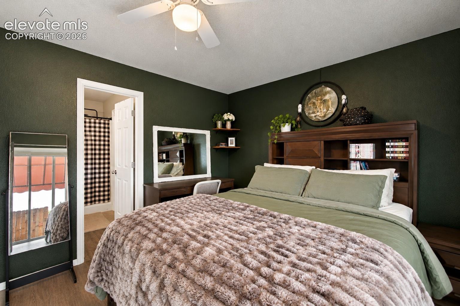 Wood-finish flooring, ceiling fan with integrated lighting, built-in shelving in headboard, and a white paneled door