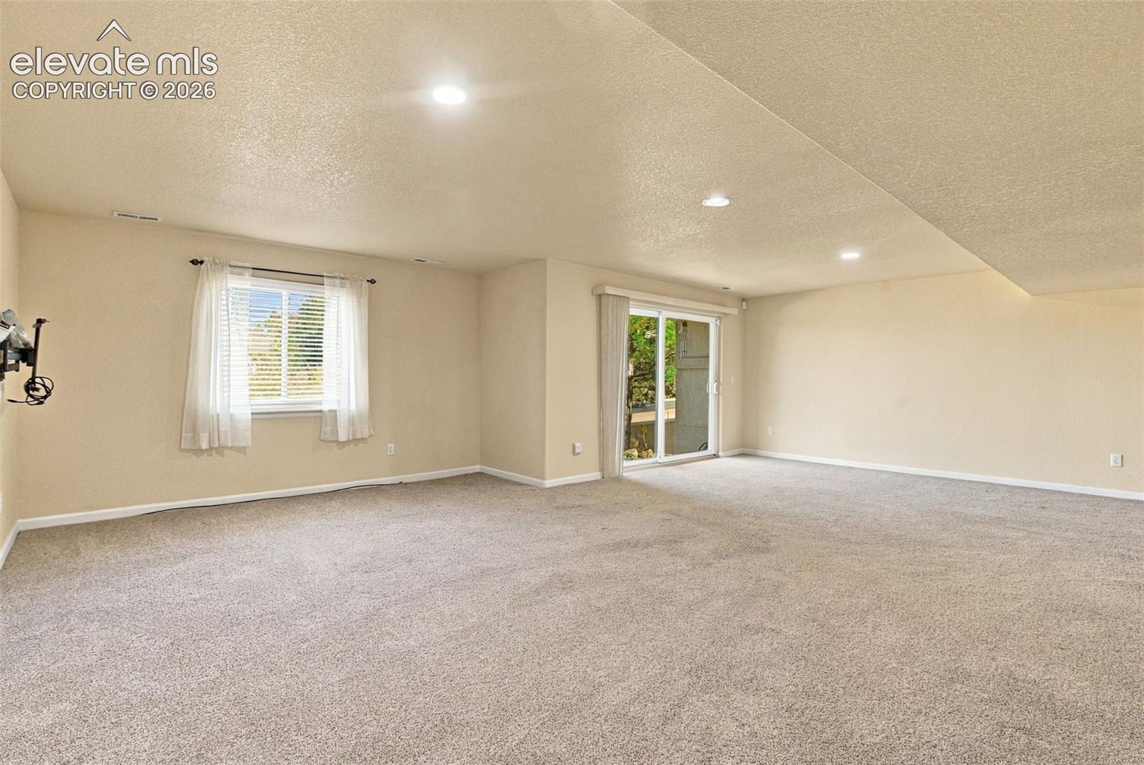 Spacious room featuring neutral carpeting, recessed ceiling lighting, a sliding glass door, and a single-pane window