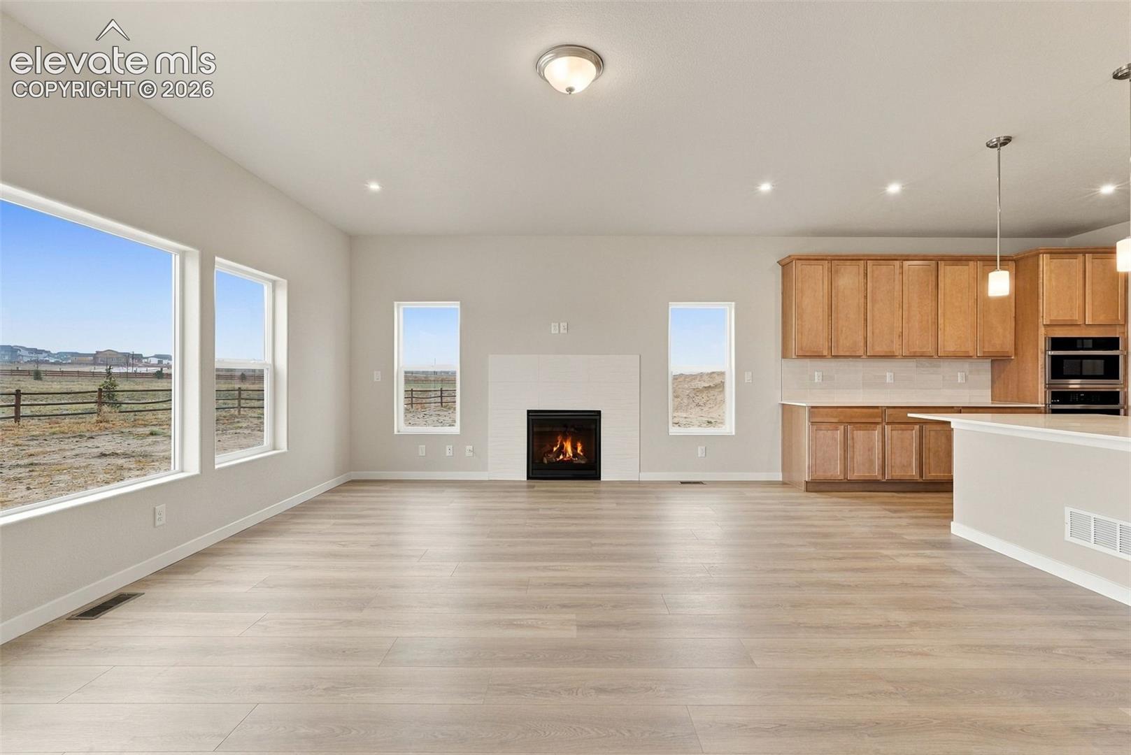 Open-concept interior featuring wood-finish flooring, a white brick fireplace, natural wood cabinetry, recessed lighting, and expansive windows
