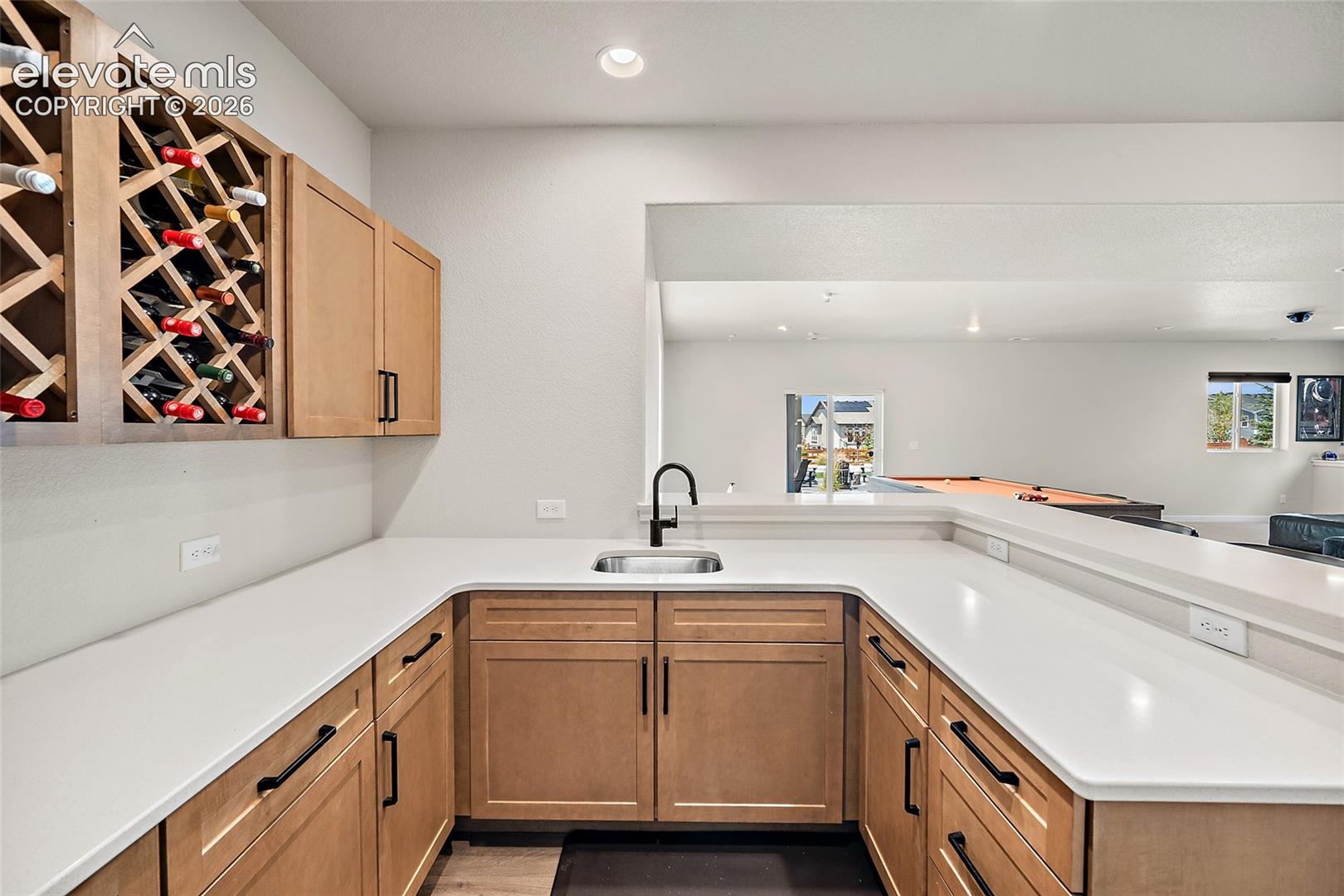 Wet bar featuring, built-in wine storage, a stainless steel sink with a matte black faucet, and light-toned countertops