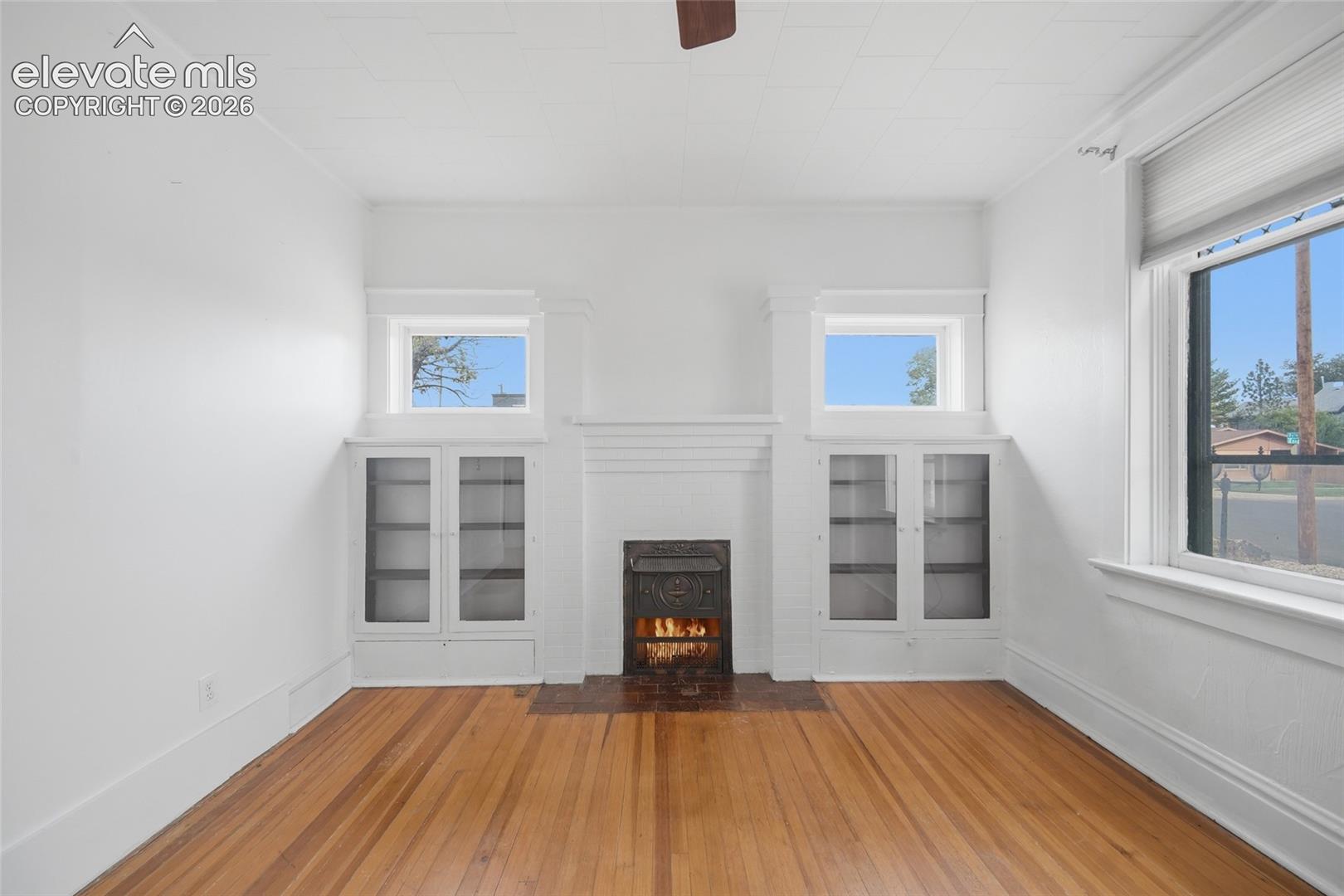 Living area featuring wood-finish flooring, a central fireplace with a decorative metal insert, and built-in cabinetry with glass-front upper doors