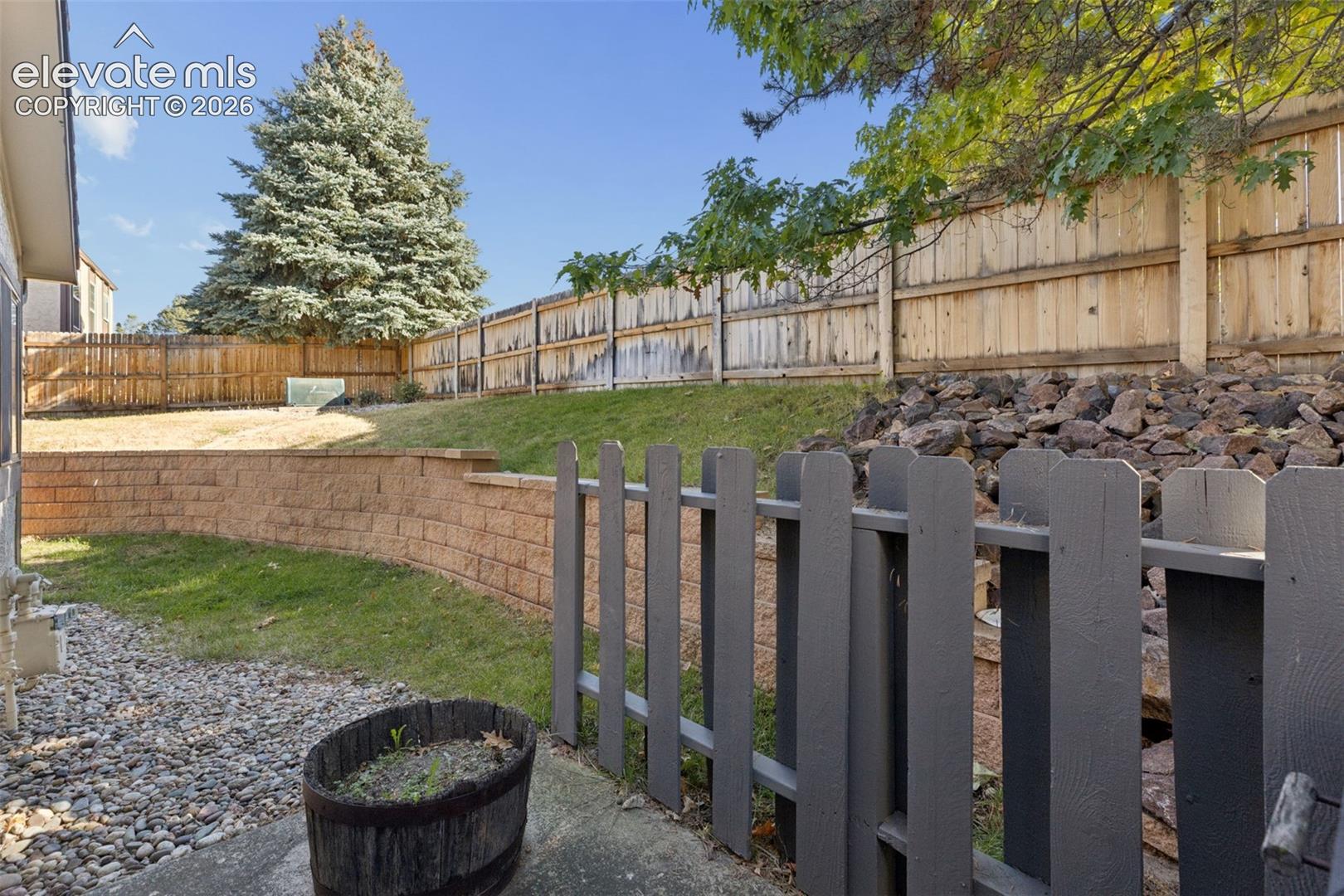 Tiered backyard featuring a stone retaining wall, wooden privacy fencing, a graveled ground cover, and a manicured lawn area