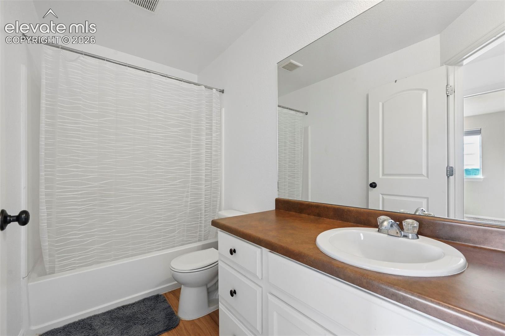 Bathroom featuring a vanity with a solid-surface countertop and integrated sink, white cabinetry with matte black hardware, and a tub-shower combination with a full-width wall mirror