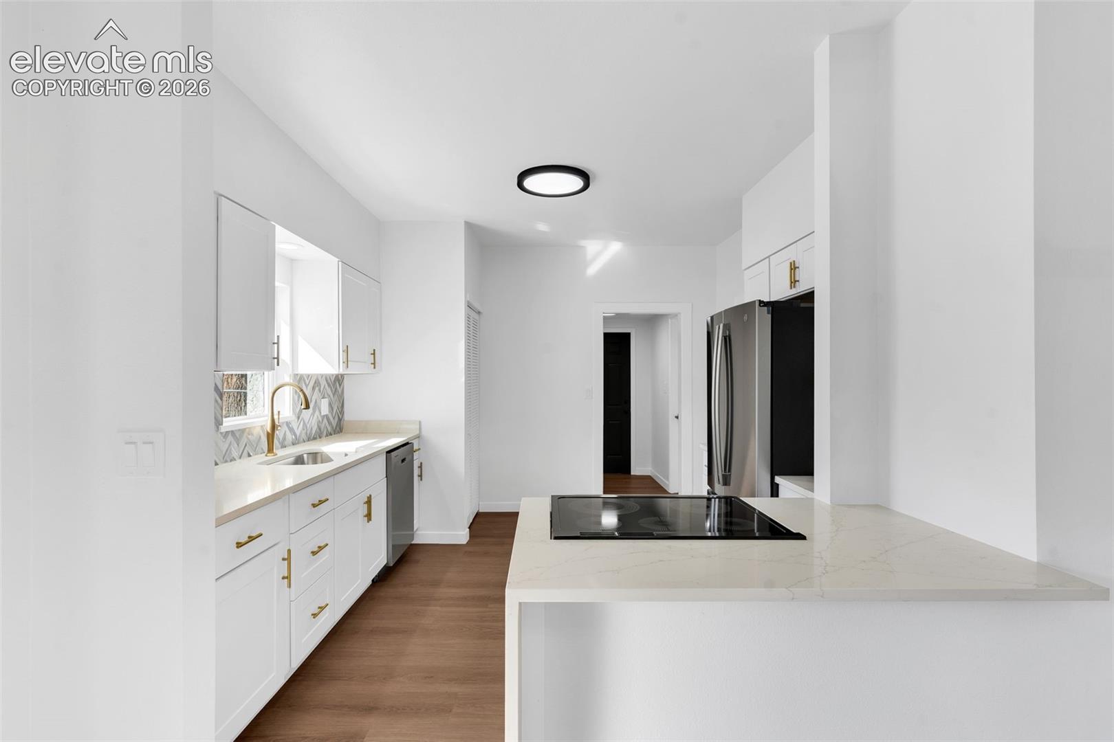 Kitchen featuring white shaker cabinetry, stone-surface countertops, herringbone-patterned backsplash, stainless steel appliances, and wood-finish flooring