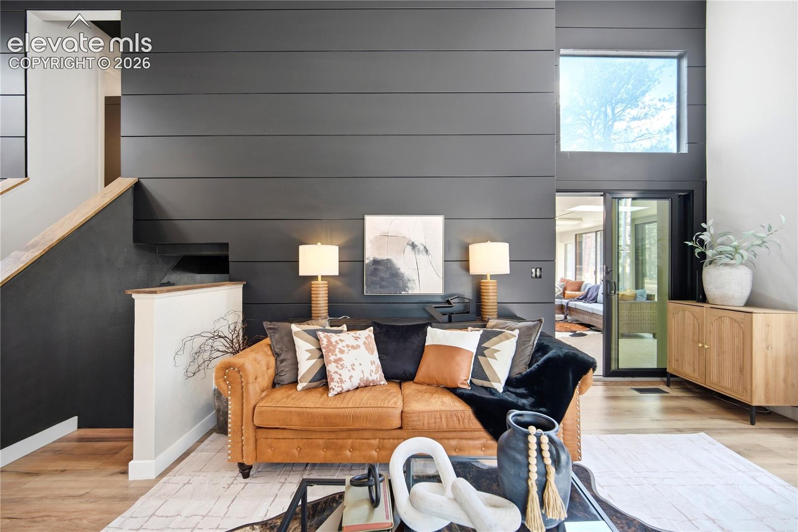 Interior space featuring a full-height charcoal shiplap accent wall, high ceilings, wood-finish flooring, a contemporary staircase with a wooden handrail, and a fixed transom window