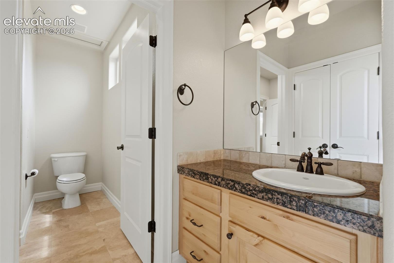 Bathroom featuring a natural wood vanity with dark hardware, a surface-mounted sink, and a dark stone countertop with a matching backsplash