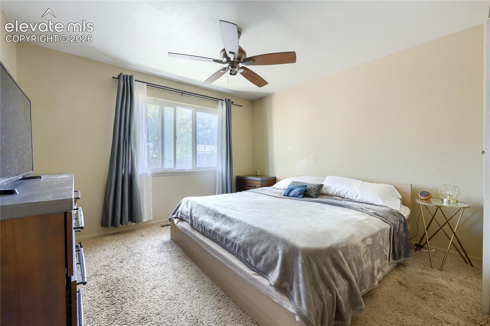 Bedroom featuring neutral wall paint, wall-to-wall carpeting, a multi-blade ceiling fan, and a horizontal window with hardware for window treatments