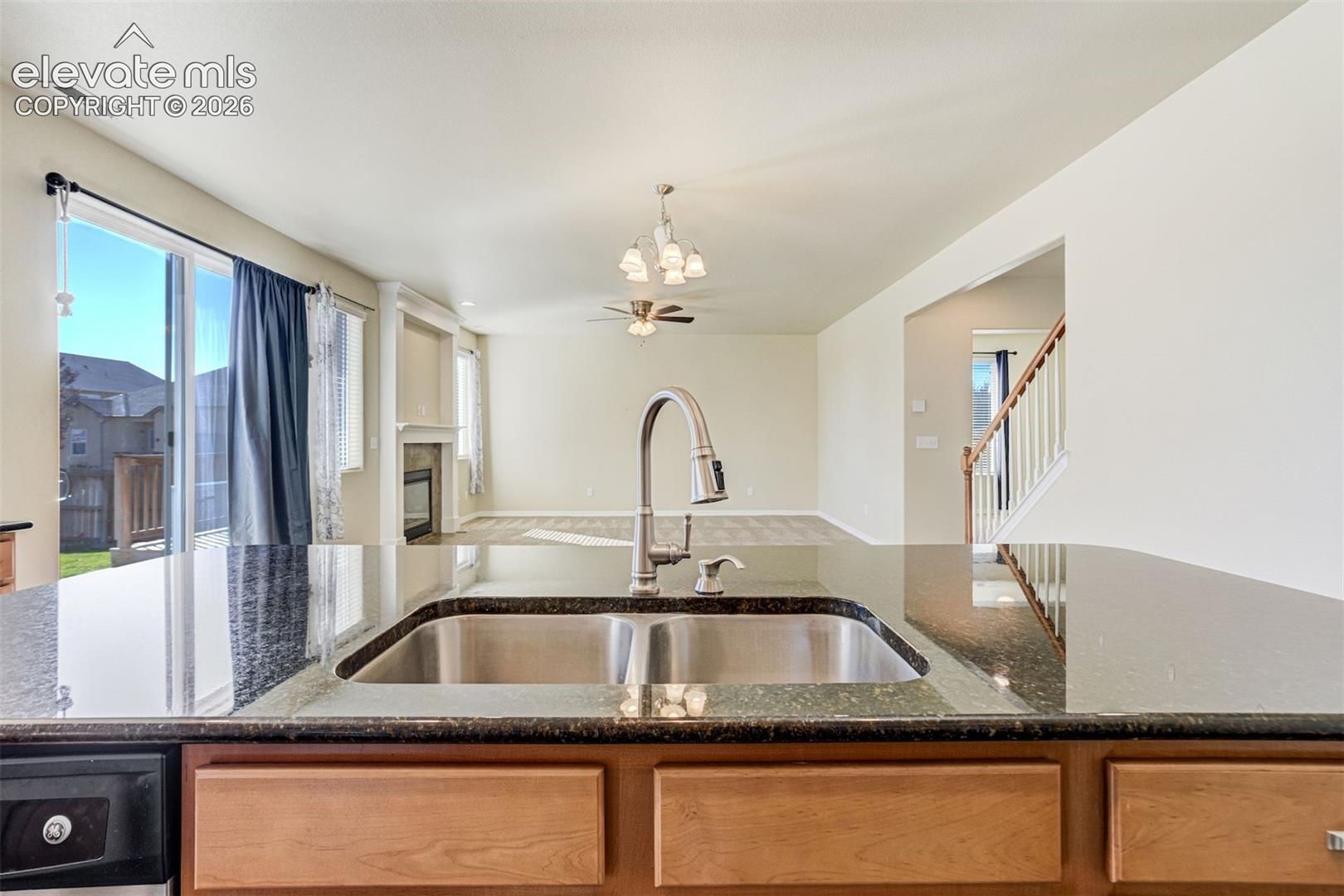 Kitchen island featuring a double basin stainless steel sink with a gooseneck faucet, set within dark granite-finish countertops and wood-finish cabinetry