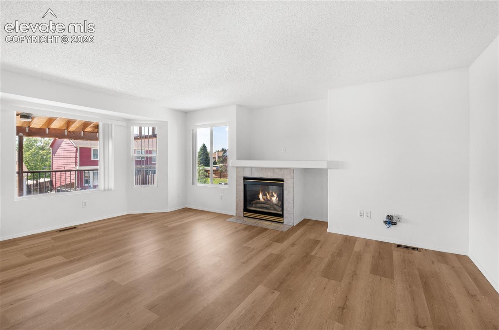 Wood-finish flooring throughout, a gas fireplace with a tiled surround, and a wide bay window