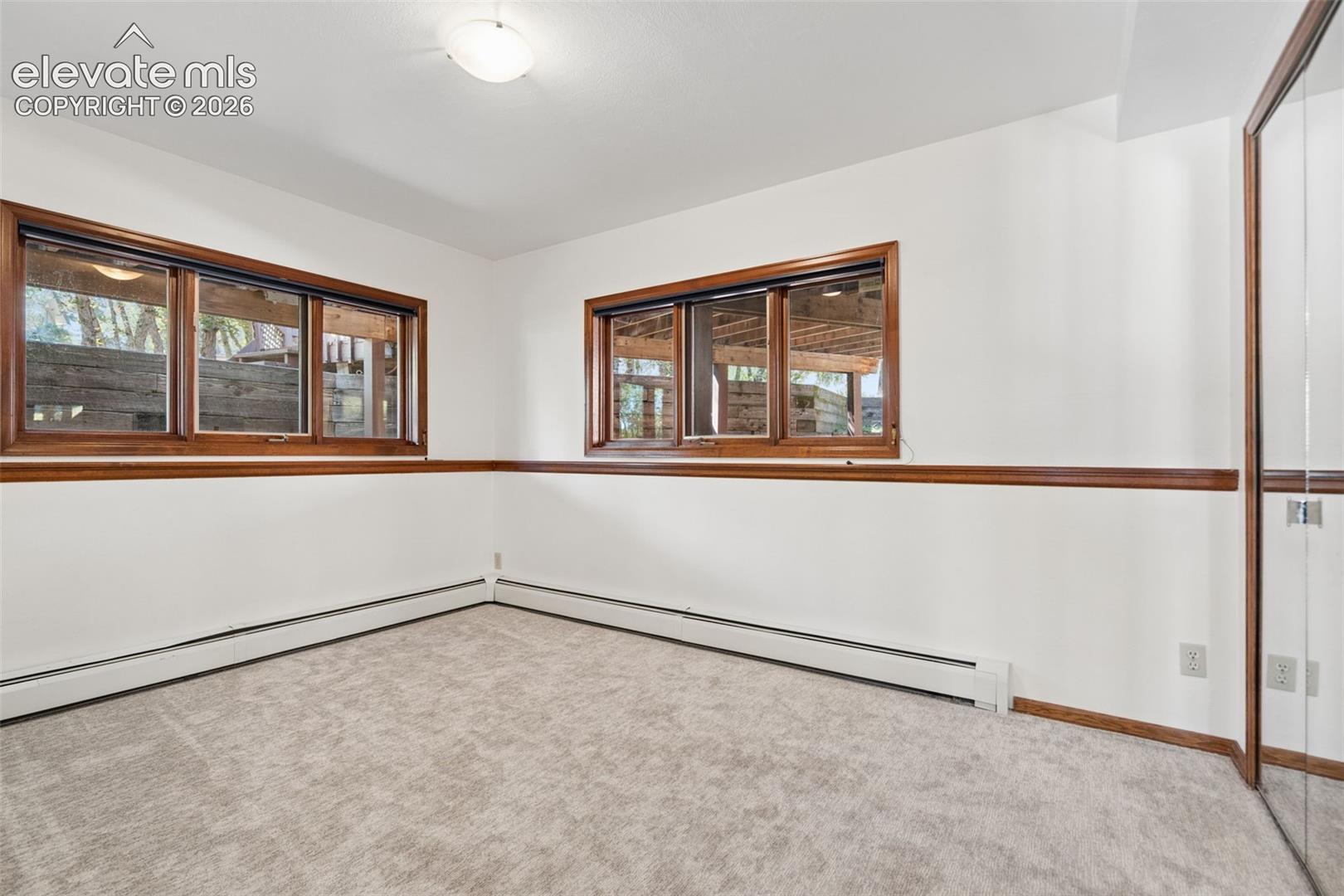 Light-colored carpeting, white painted walls, wood-finish window trim, multiple windows, and a mirrored closet door