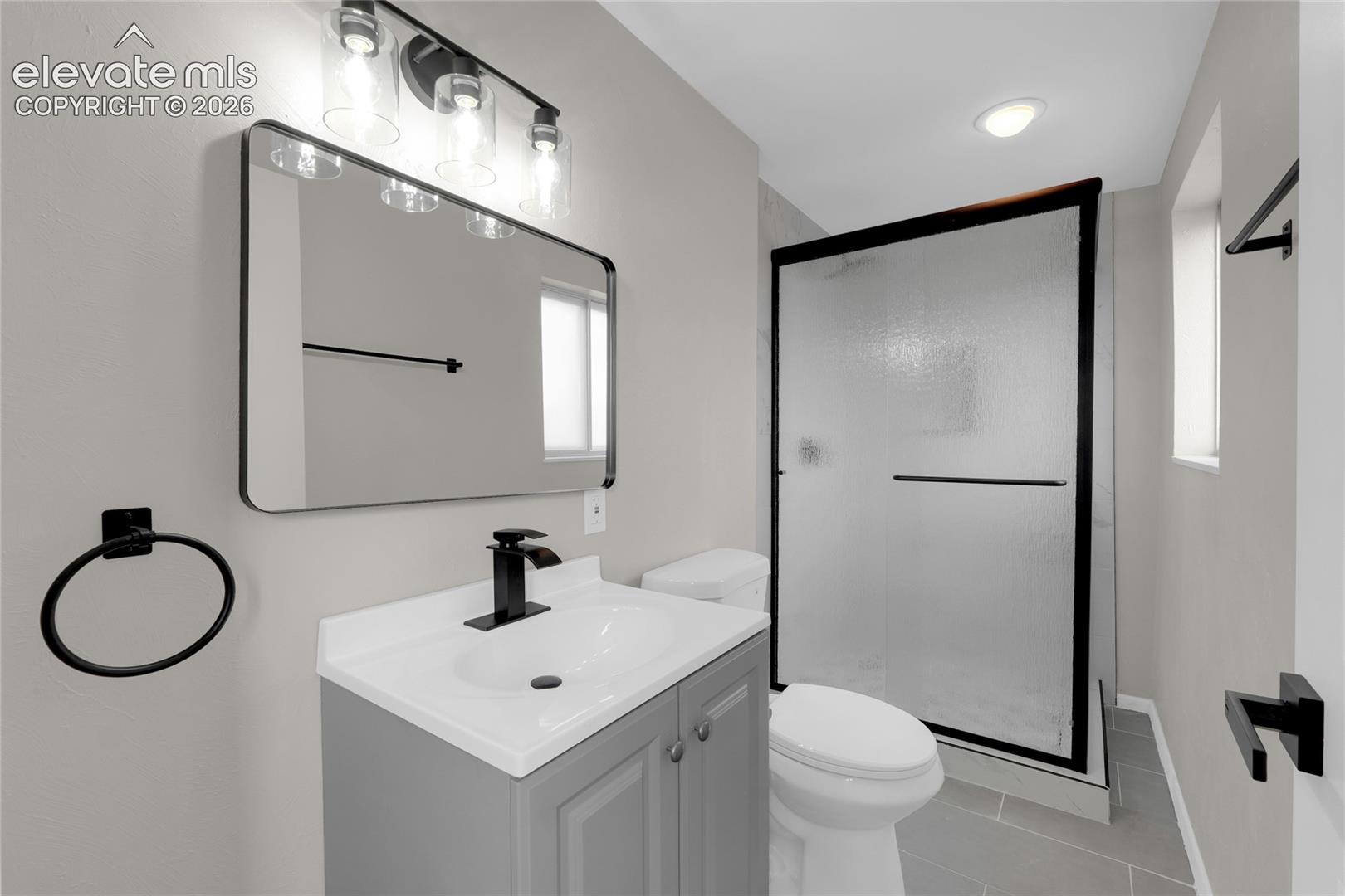 Bathroom featuring a single vanity with an undermount sink, a shower enclosure with a sliding frosted glass door, and matte black fixtures