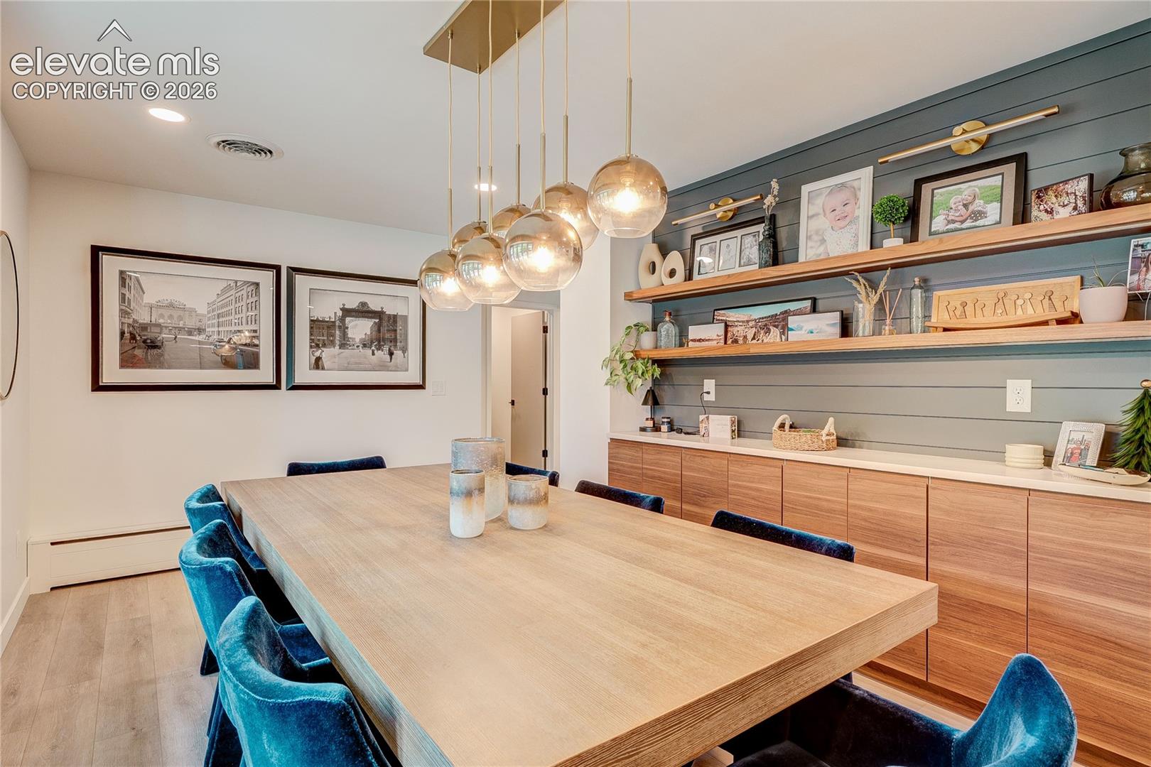 Gold-finish linear chandelier with glass globes, wood-finish flooring, recessed lighting, and built-in wood cabinetry with open shelving