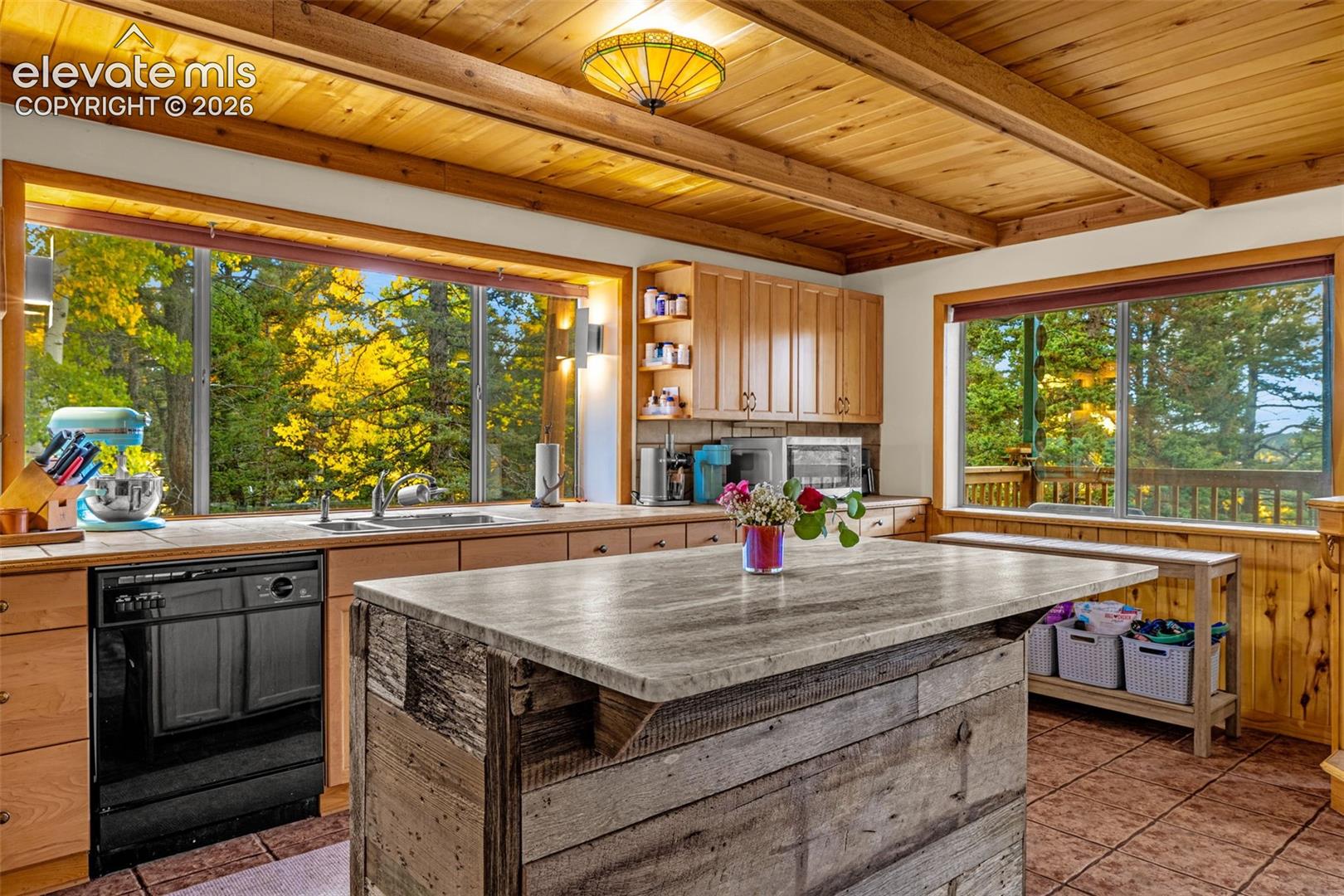 Kitchen featuring a center island with a stone-finish countertop and weathered wood base, natural wood-paneled ceiling with exposed beams, tile flooring, and large picture windows